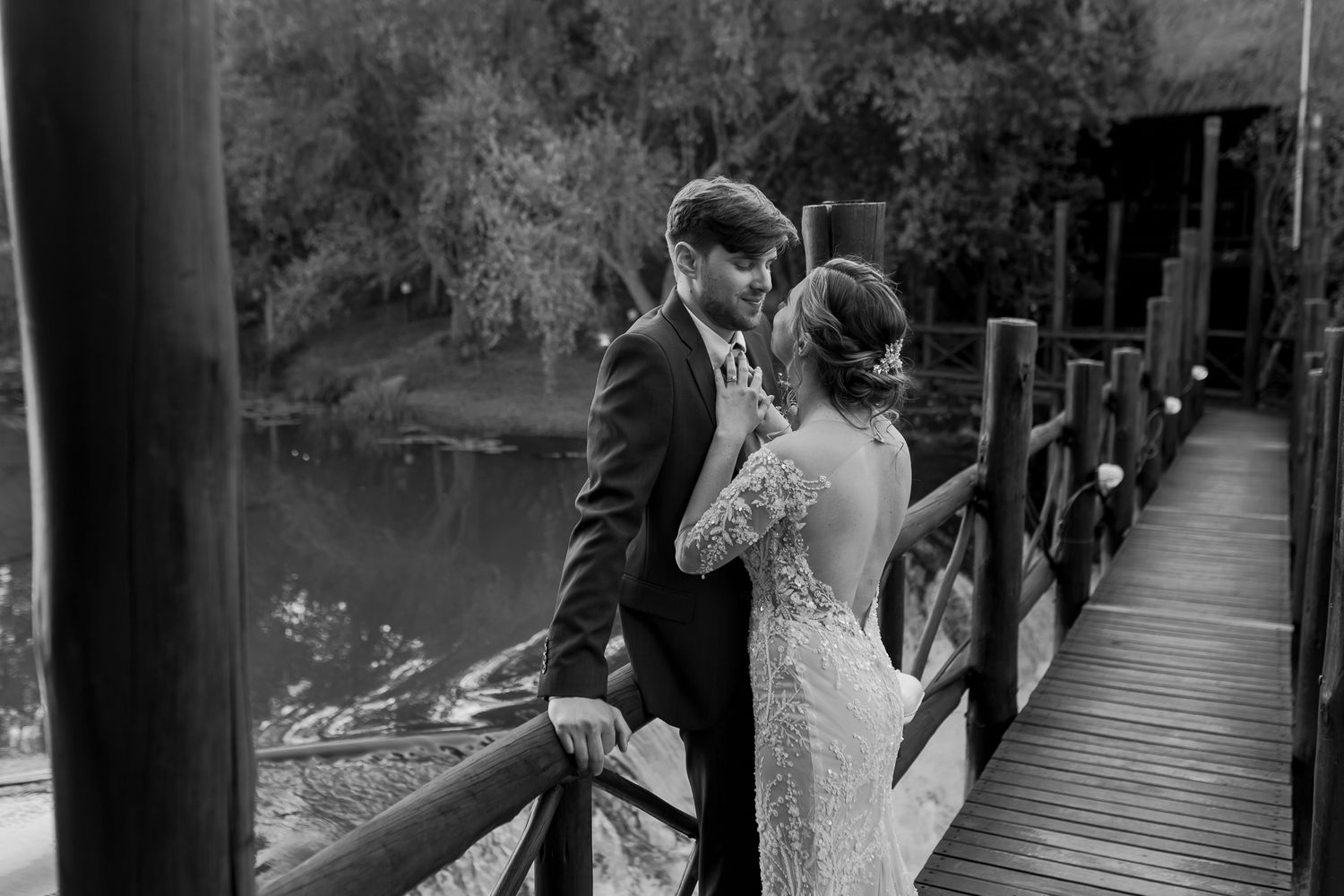 A romantic black and white photo of newlyweds sharing an intimate moment on a wooden bridge.