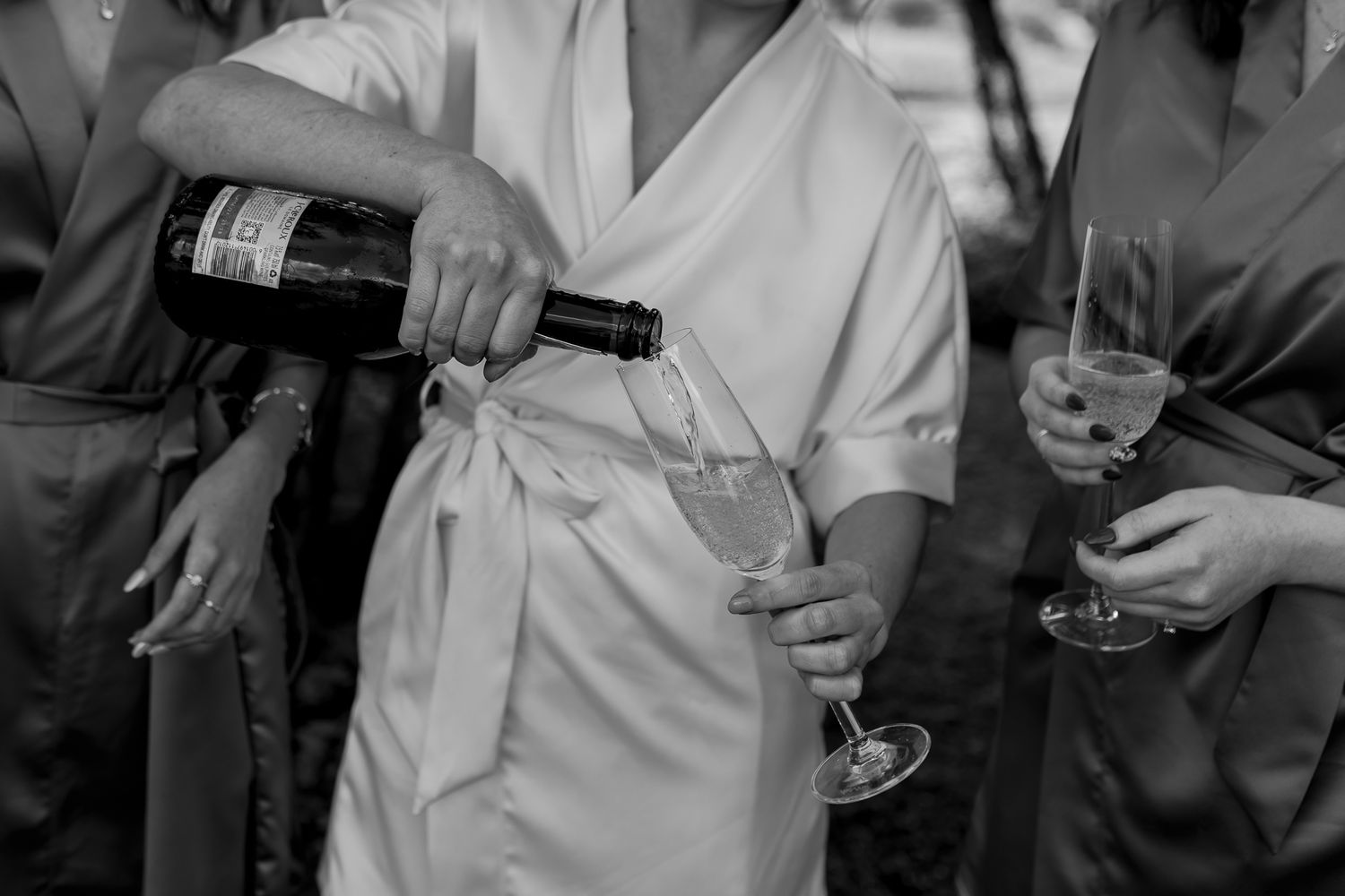 A person in a white robe pours champagne into a glass at a celebration.