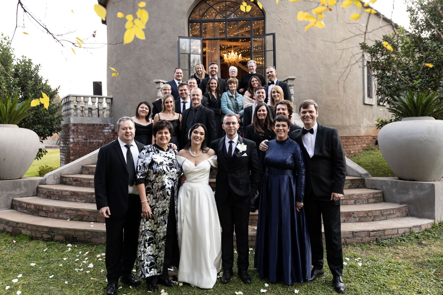 Wedding party gathered at entrance steps of historic stone building with yellow flowers blooming above arched doorway.