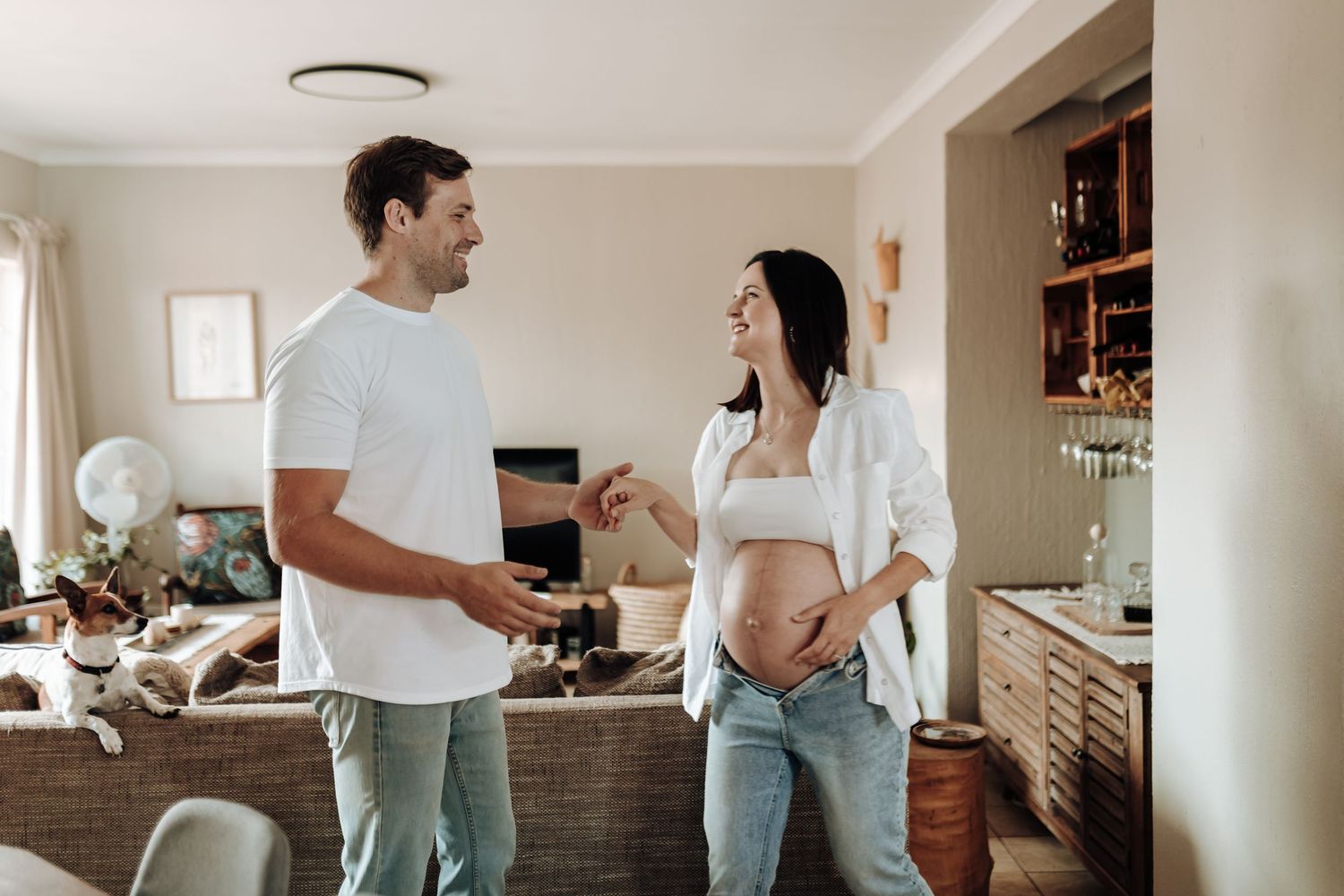 Couple in casual white tops and jeans enjoying playful moments together in their living room.