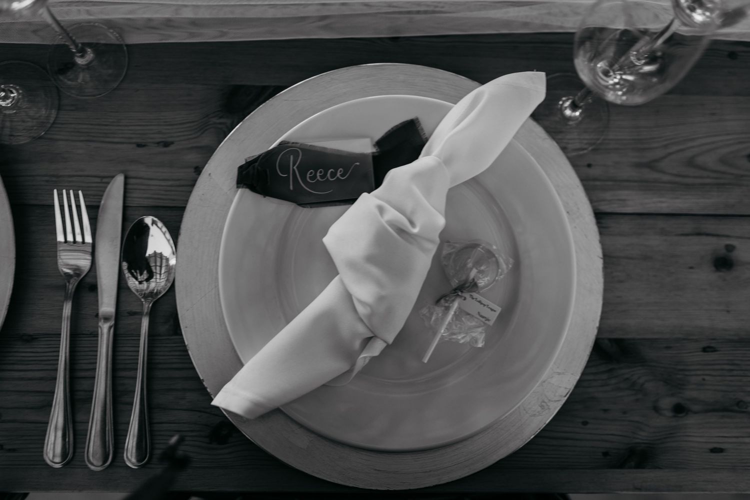 Black and white photo of elegant table settings with plates, silverware and napkins arranged on a rustic wooden surface.