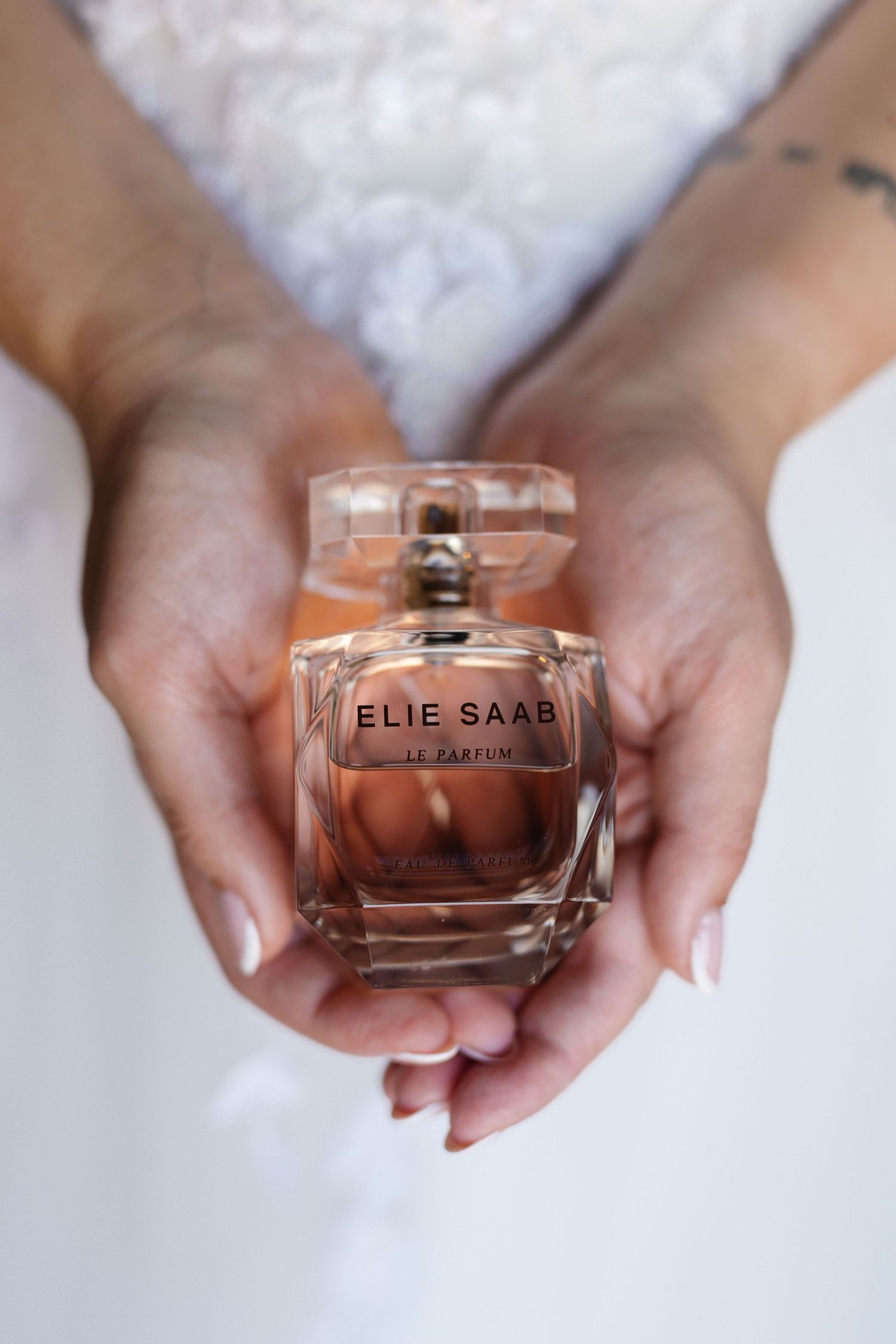 Hands holding an Elie Saab perfume bottle against a white background, shown in a sequence of four similar shots.