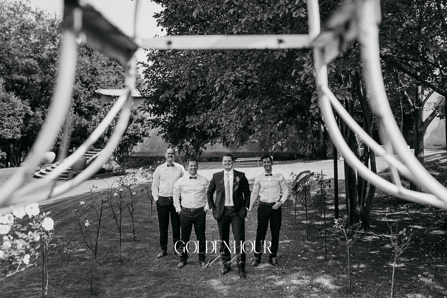 Black and white photo of groom and groomsmen standing together in a garden at a wedding.