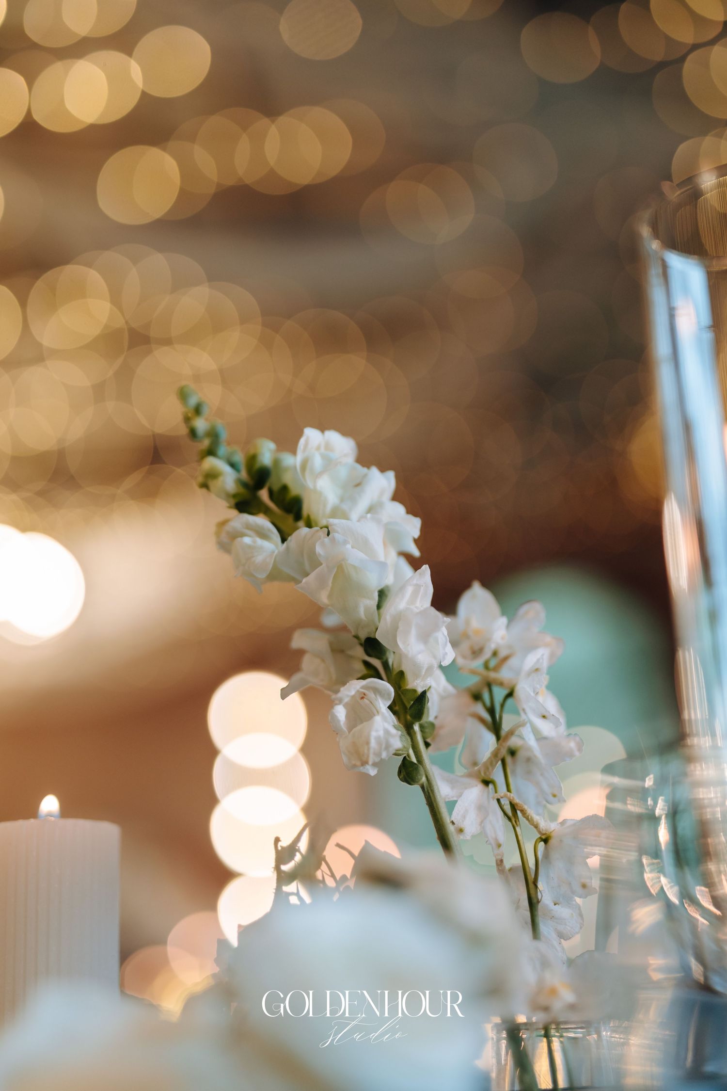 White orchids and candles create an elegant table setting with soft bokeh lighting in the background.