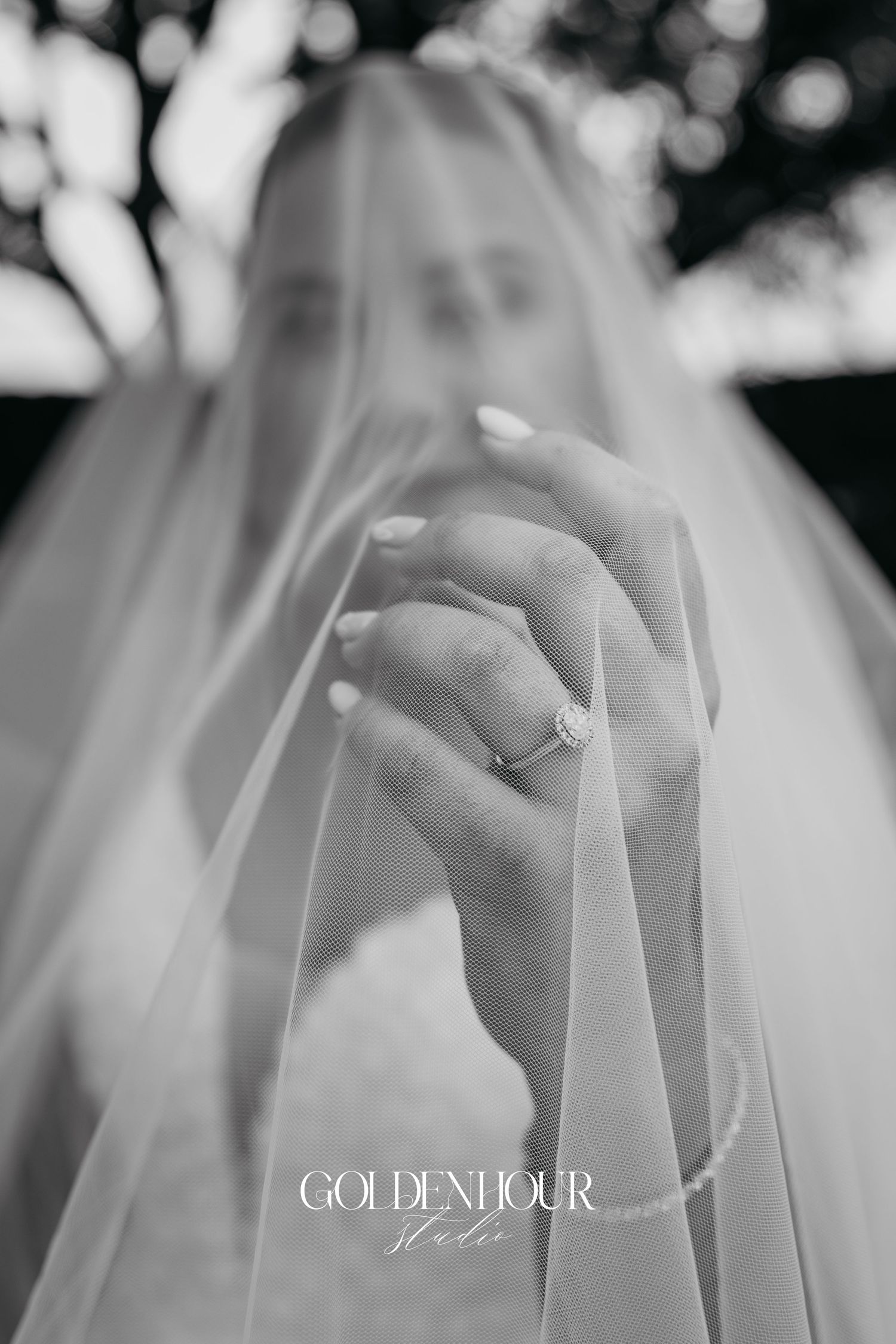 Black and white close-up of hands showing wedding rings and delicate veil details.