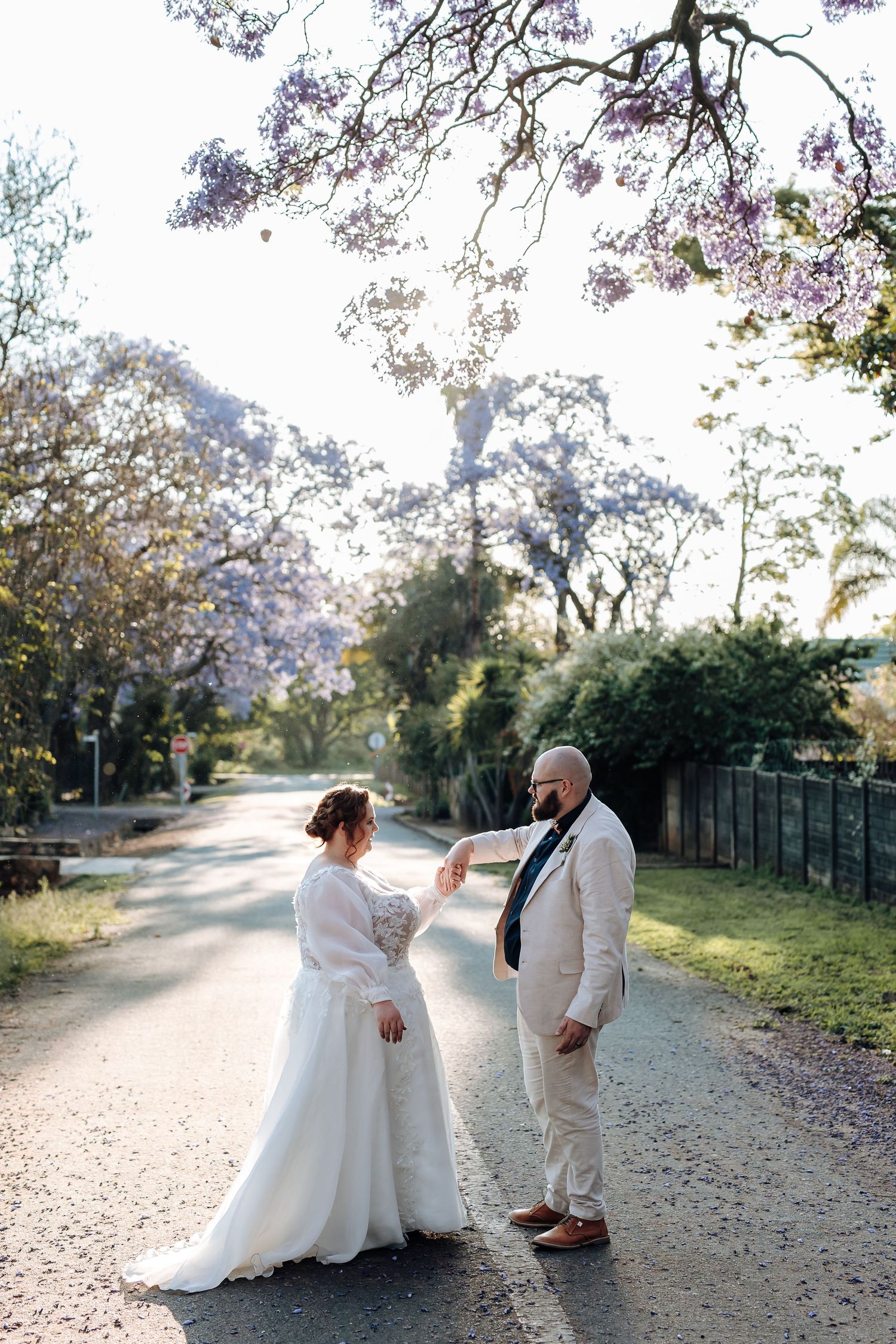 Bride and groom share a tender moment walking together on a tree-lined path during their autumn wedding celebration.