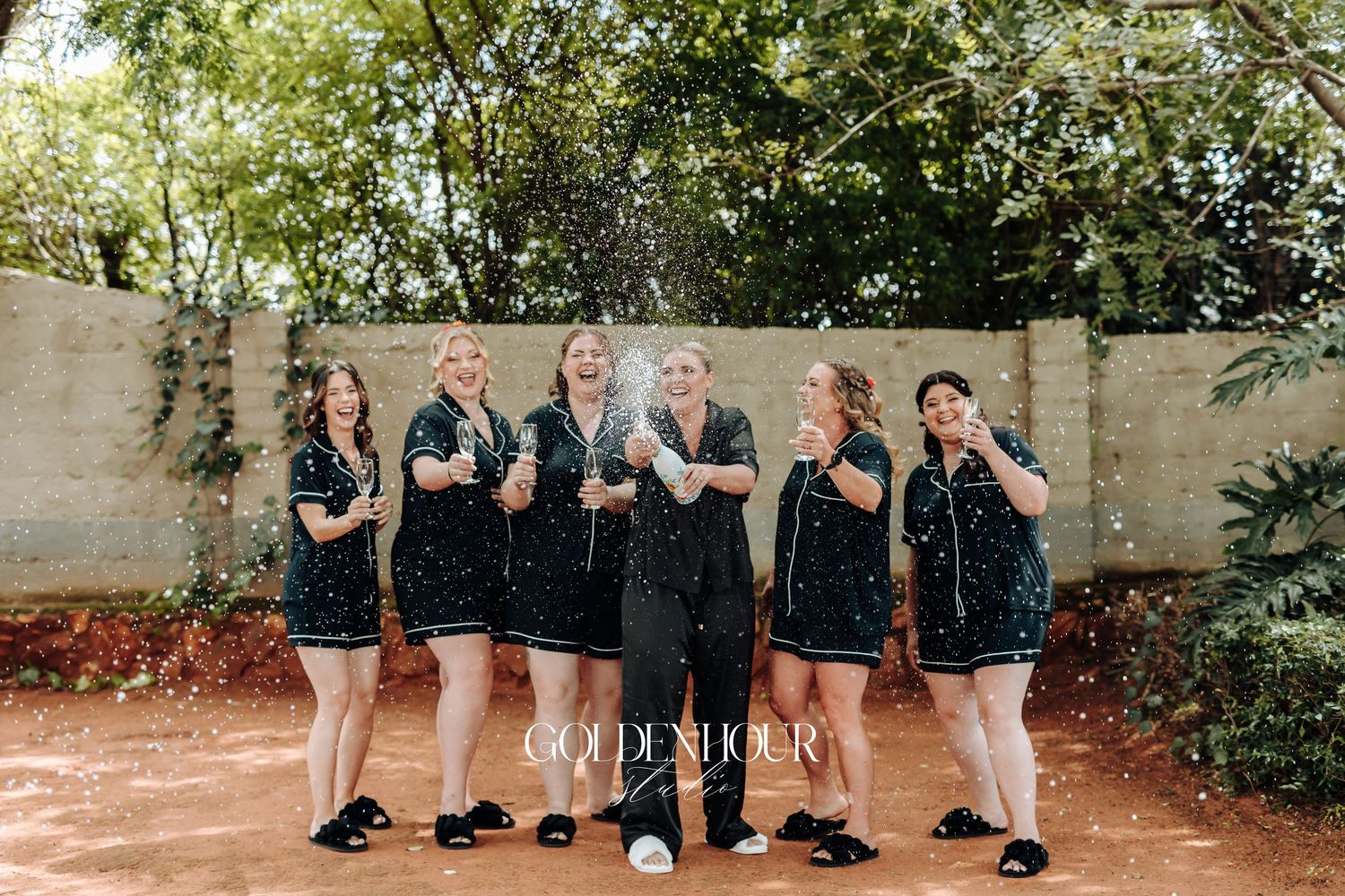 A group of people wearing black and white outfits pose together against a stone wall in an outdoor setting.