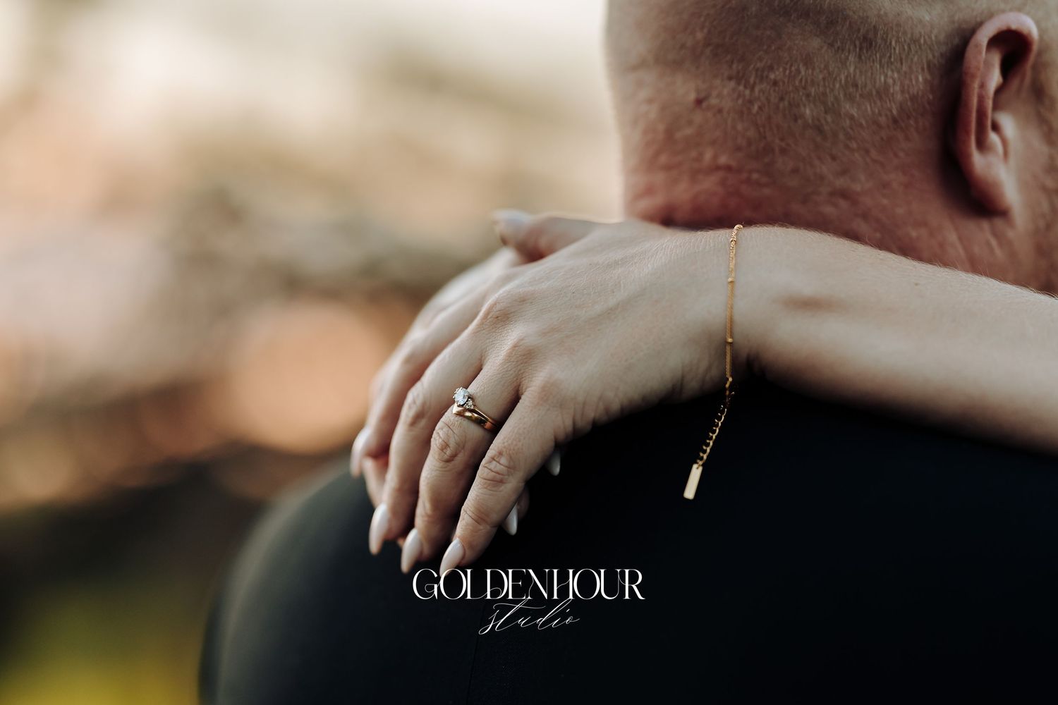 A couple holds hands while wearing wedding rings in a romantic outdoor setting during golden hour.
