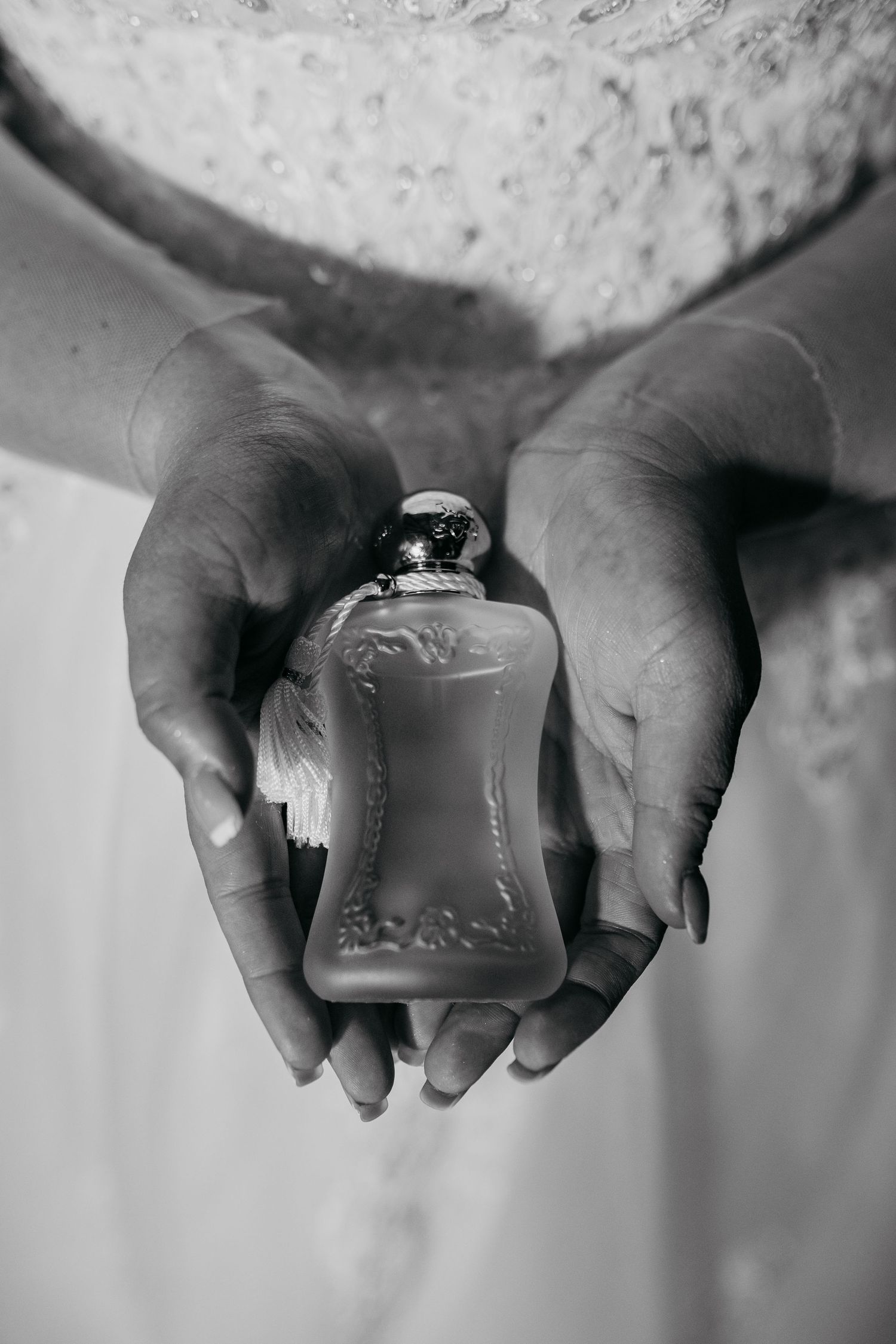 A pair of hands gently holding an ornate perfume bottle in a black and white photograph.