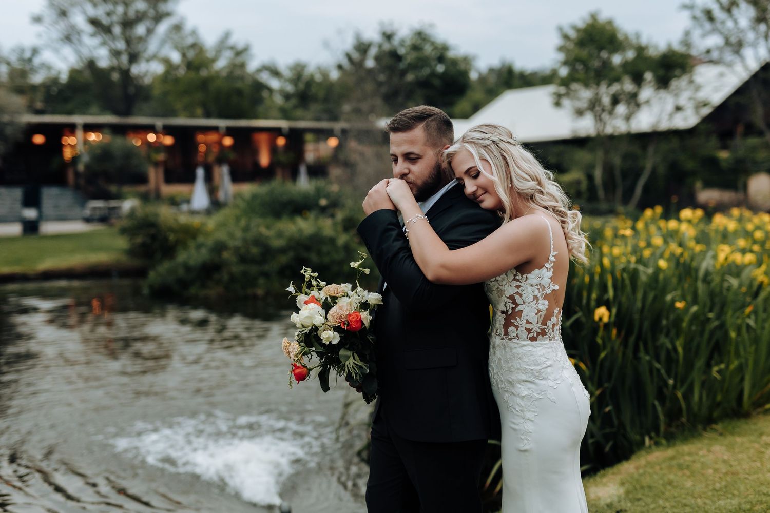 A romantic couple embraces outdoors in a garden setting with blooming flowers and natural scenery.