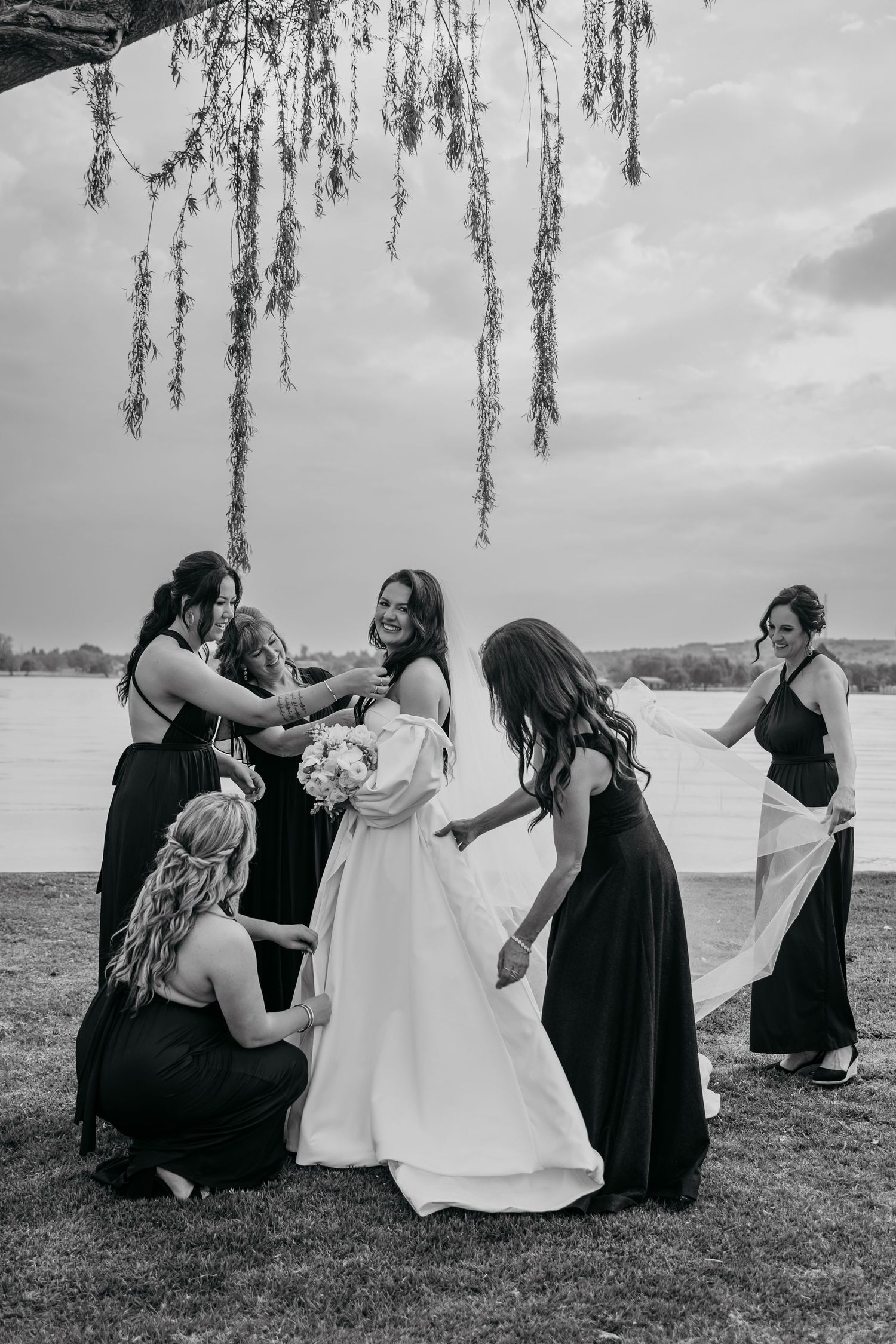 A sequence of black and white wedding photos shows a group in dark dresses helping with a white gown outdoors.