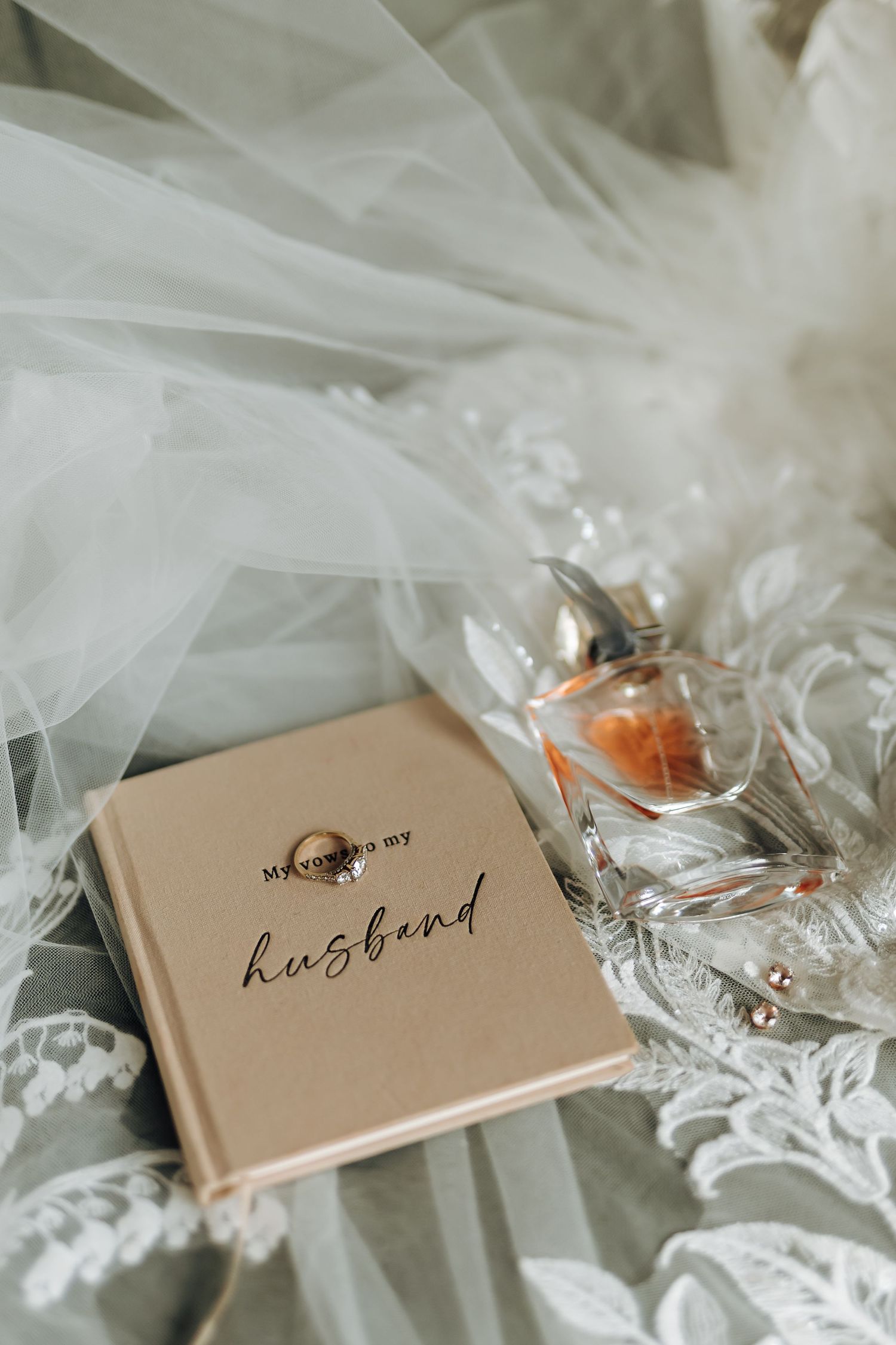 Wedding rings rest on delicate beige cards with handwritten text, surrounded by soft white tulle fabric.