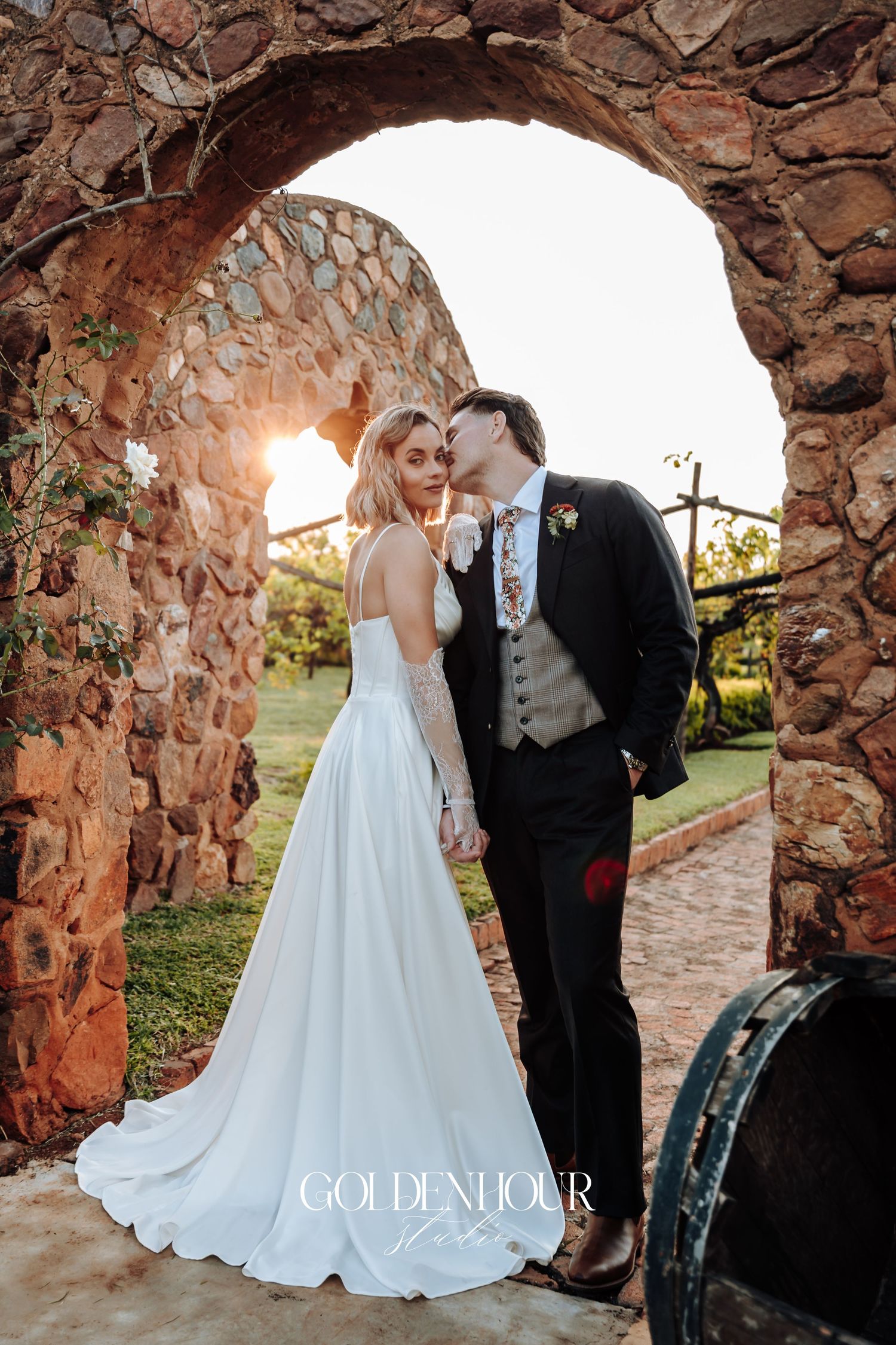 Wedding couple poses beneath rustic stone arches during sunset photo session.