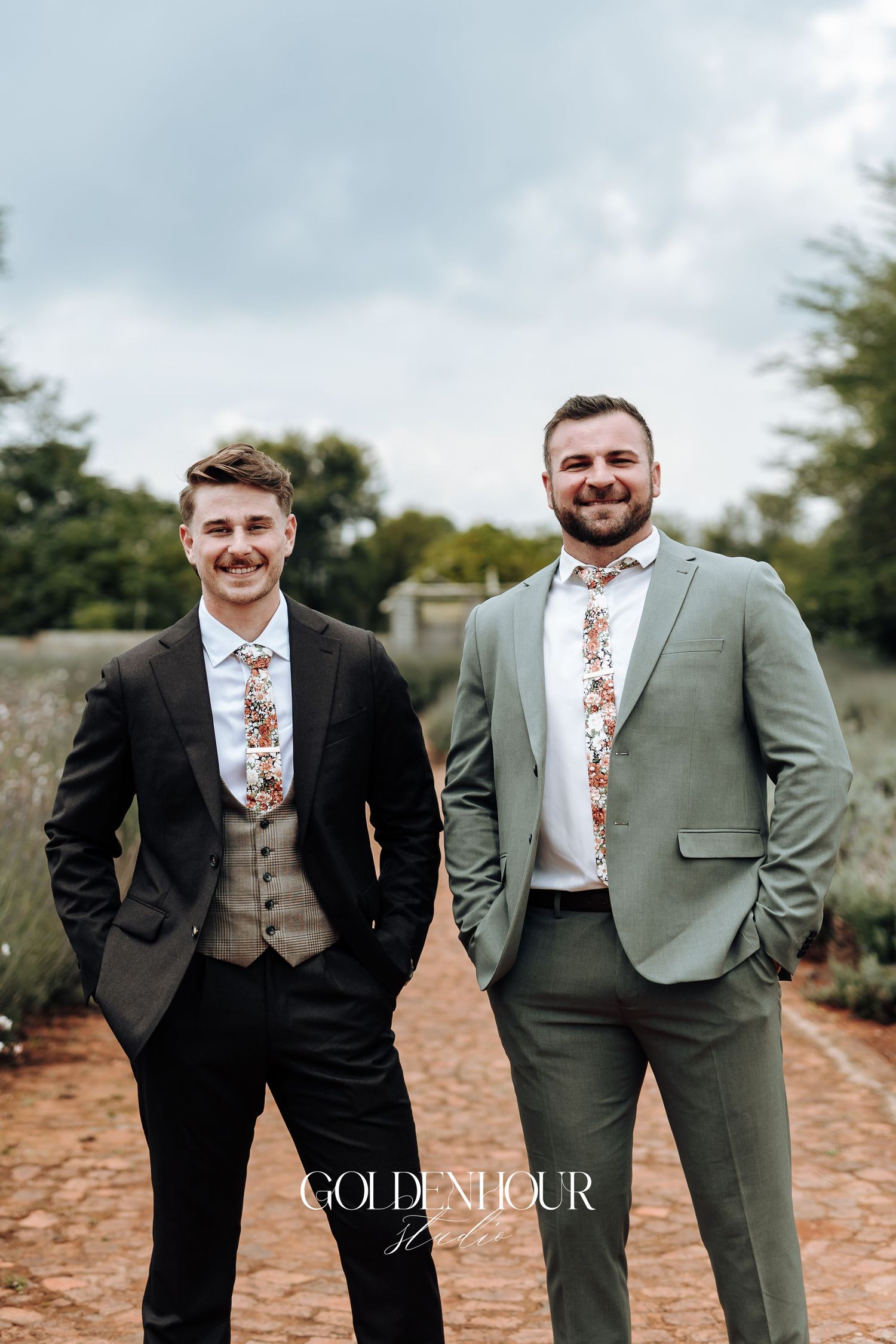 Wedding party members in sage and black suits posing together outdoors.