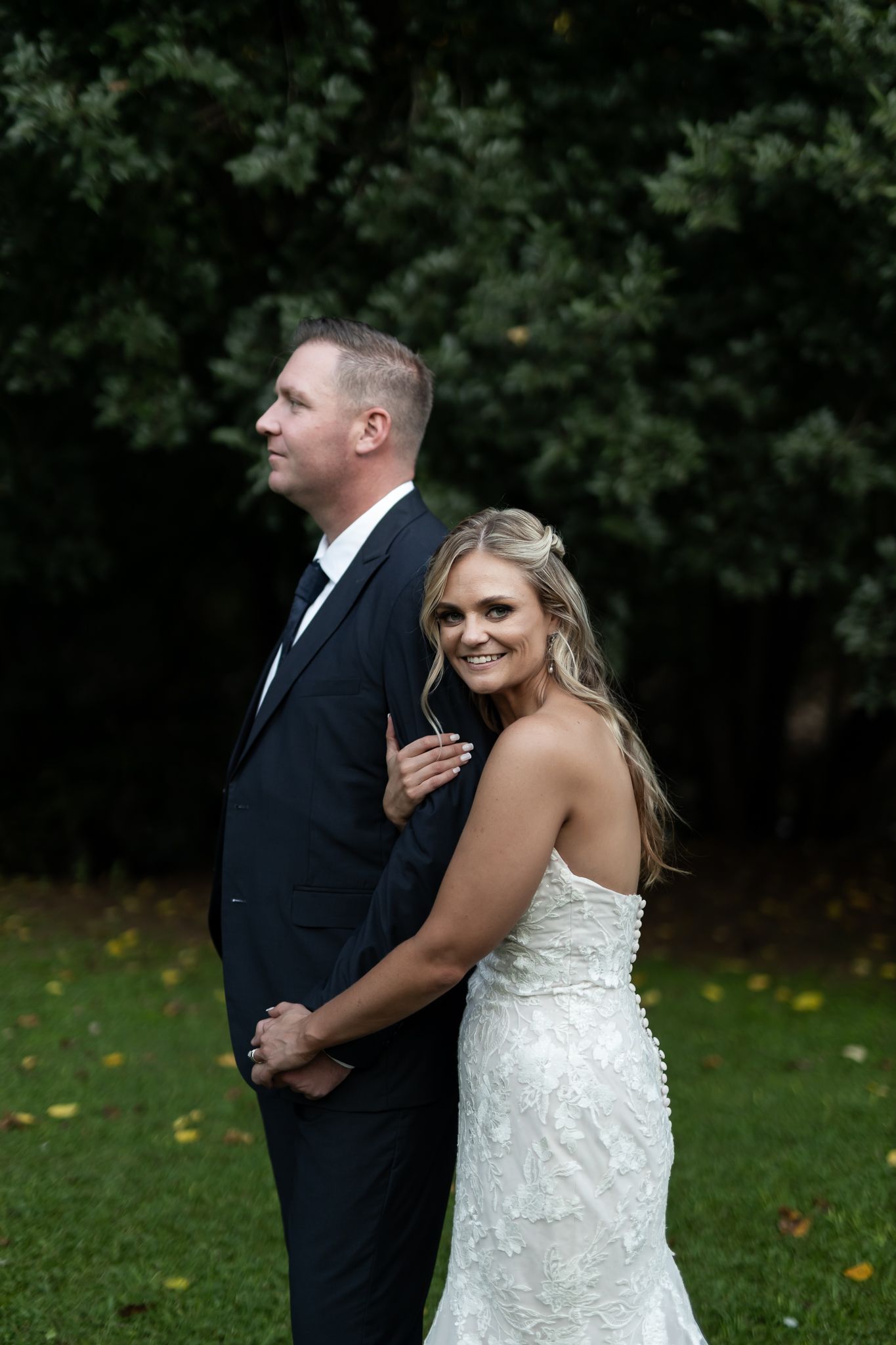 Bride embraces groom from behind during outdoor wedding portrait session.