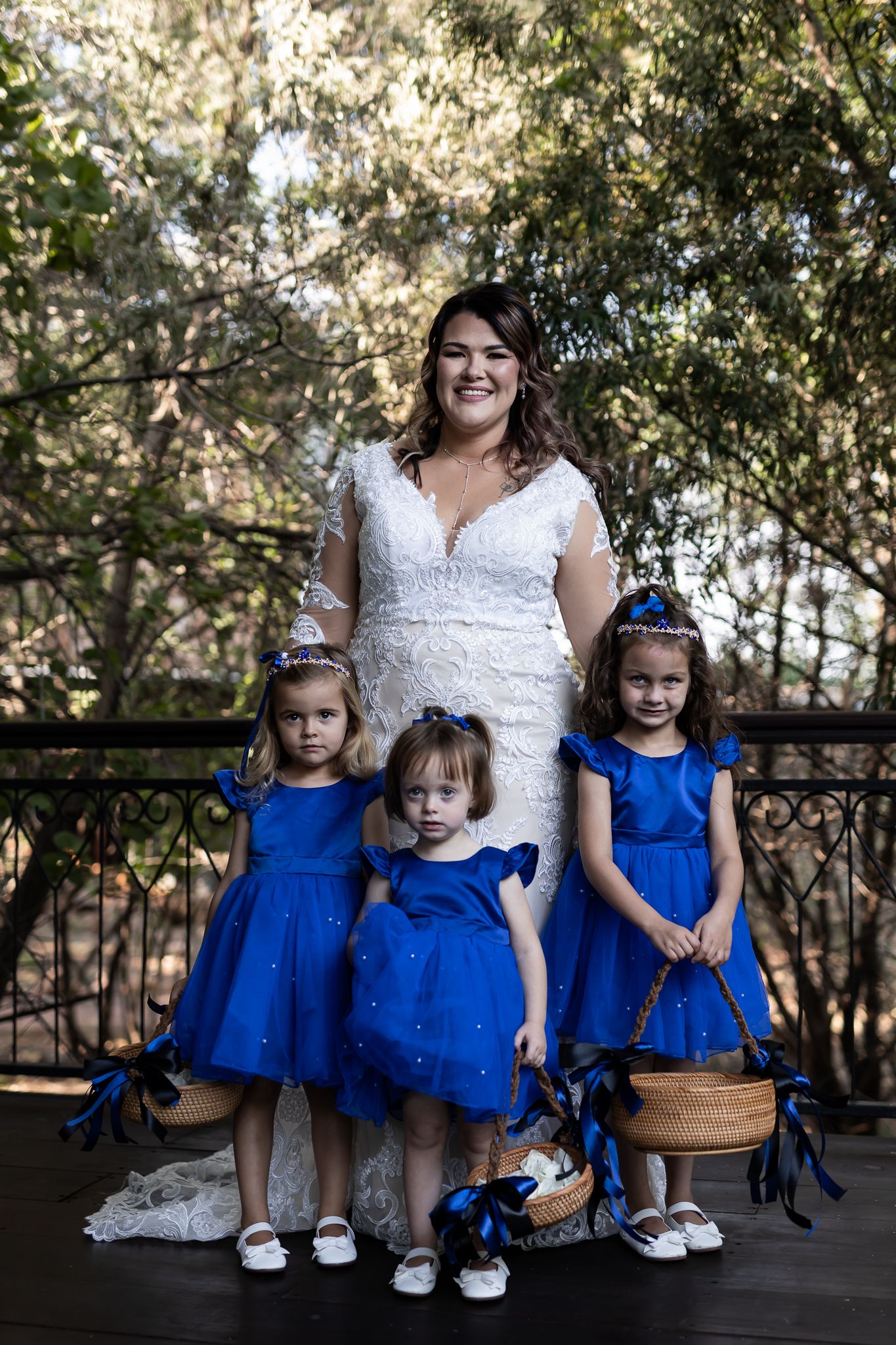A bride in white lace gown poses with three flower girls wearing matching blue dresses.