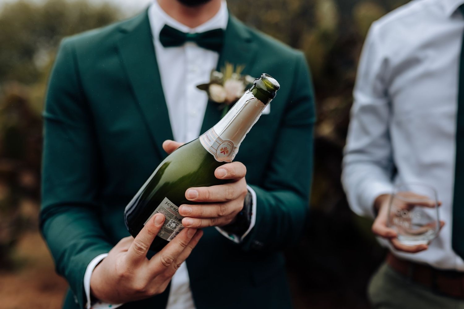 A close-up shot of a bottle of champagne being held by someone in an emerald green suit jacket.