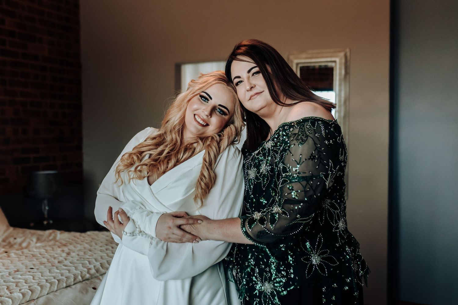Two people embrace warmly, wearing contrasting white and dark sequined dresses.