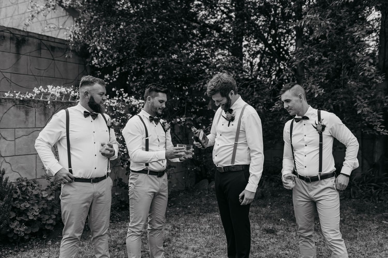 Black and white photo of groomsmen in suspenders chatting before ceremony.