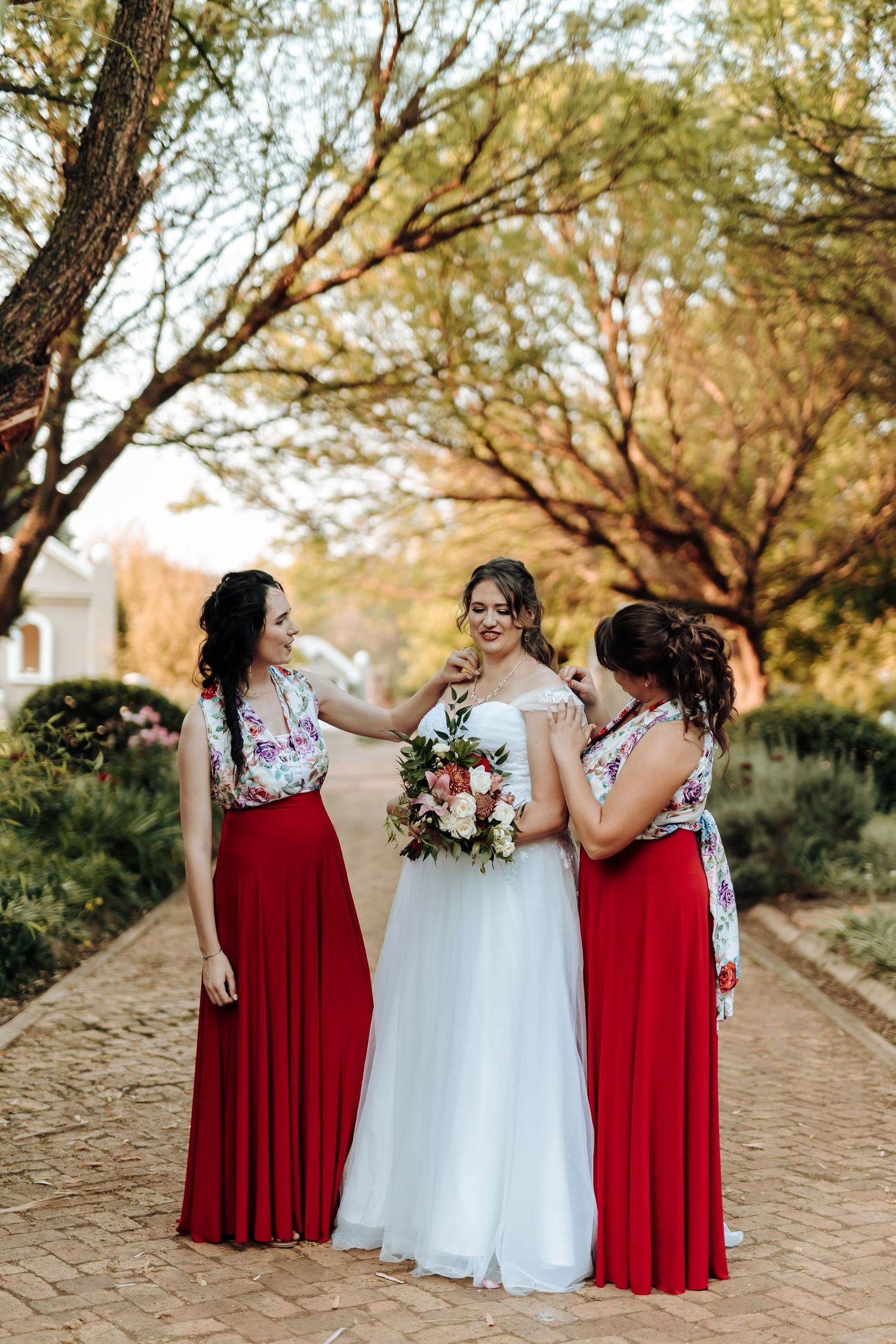 Candid moment between bridal party members in red and white dresses with bouquets.