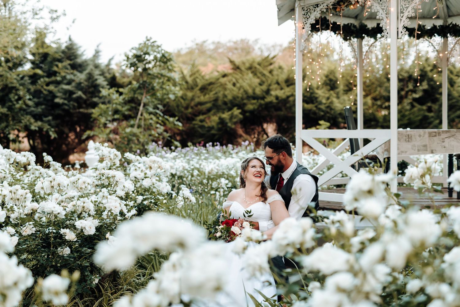 Newlyweds sharing romantic moment in blooming white flower garden under gazebo.