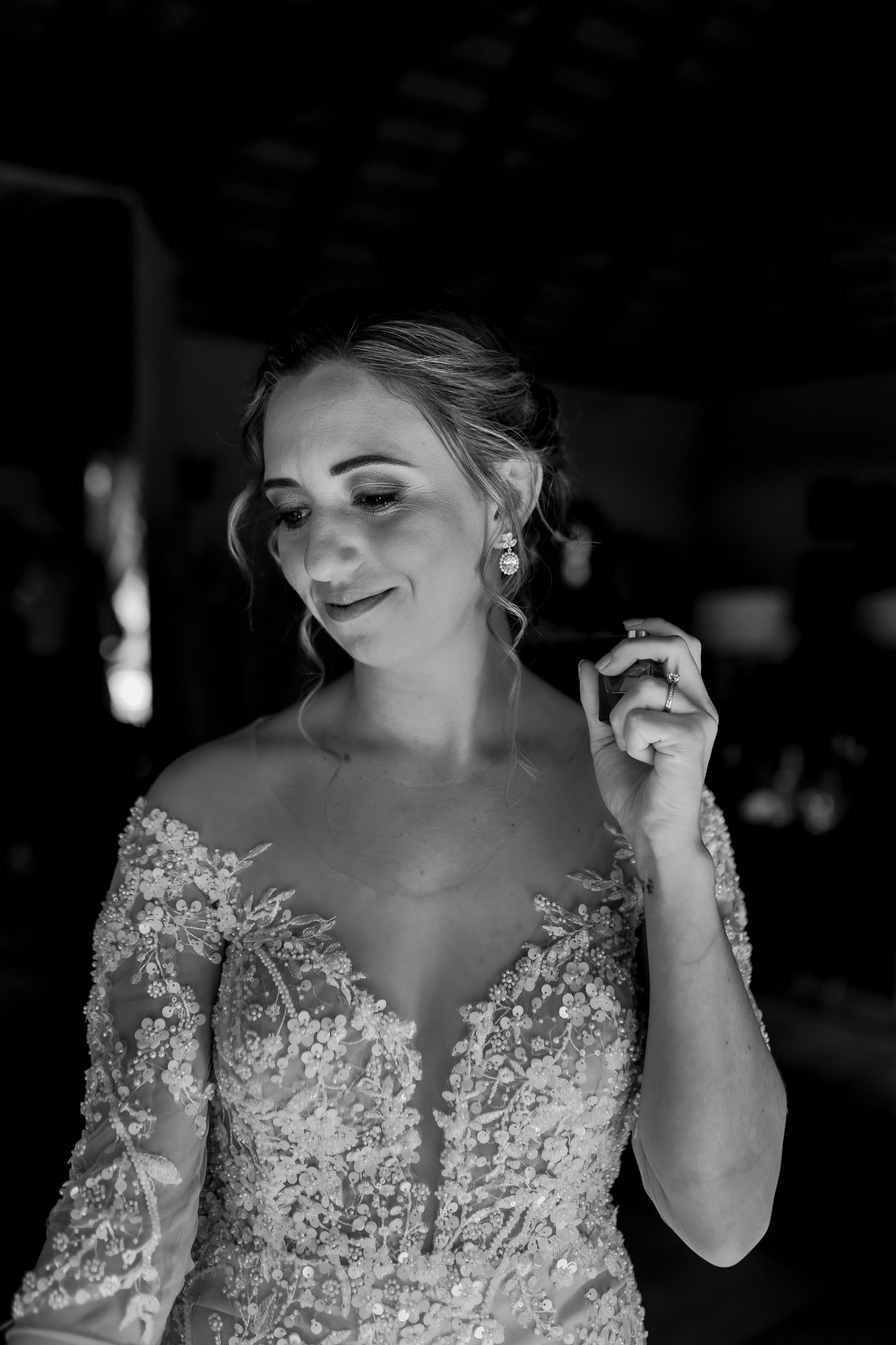 Black and white portrait of a bride in an elegant lace gown adjusting her jewelry.