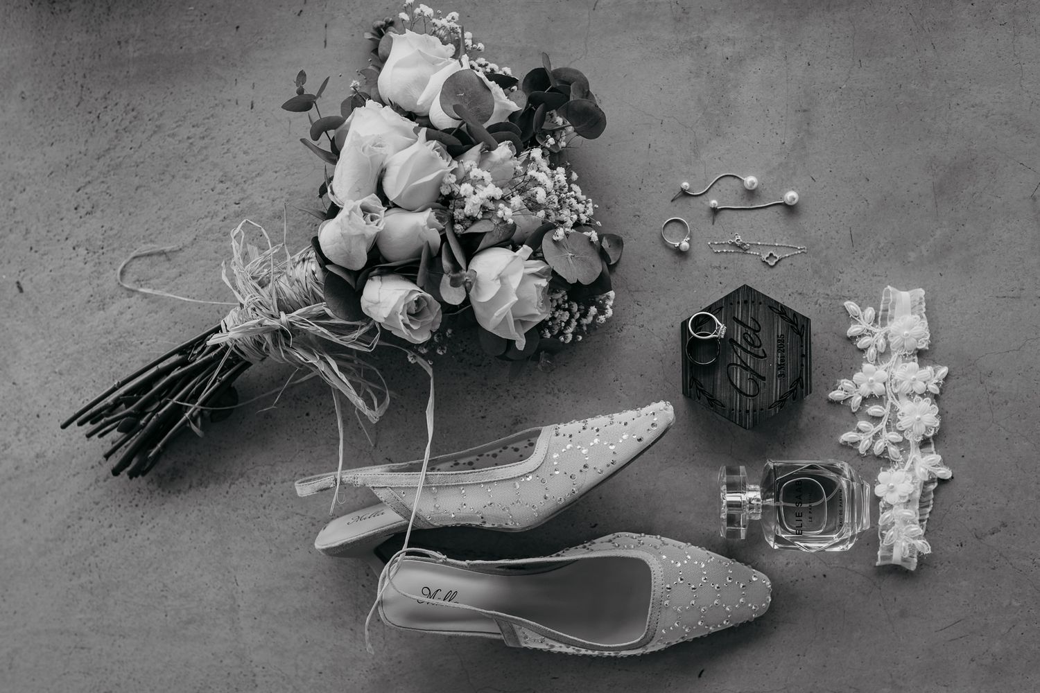 Wedding accessories including bouquet, shoes, and rings arranged in black and white.