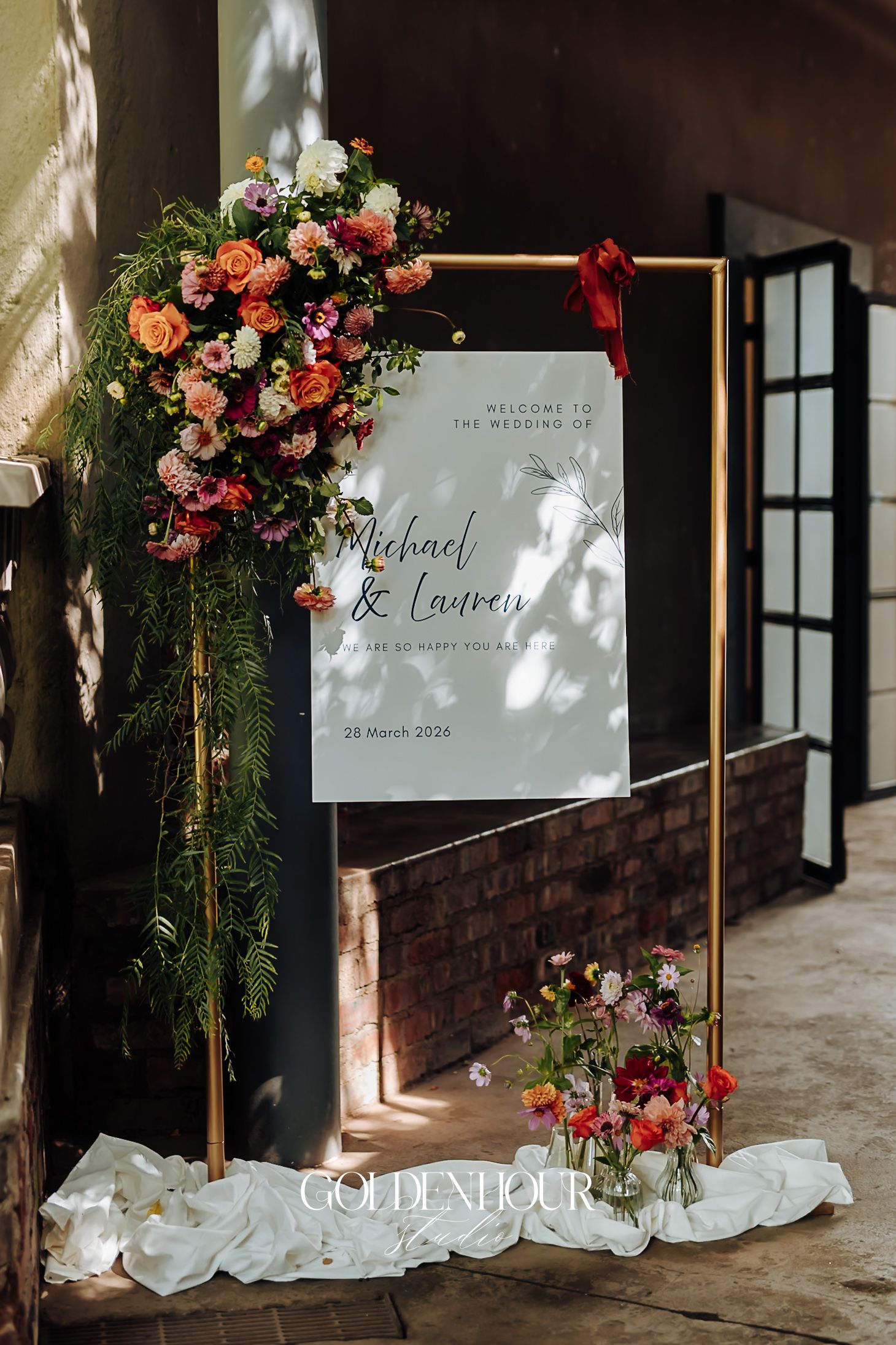 Gold wedding welcome sign with colorful floral arrangement for Michael and Lauren, 29 March 2024.