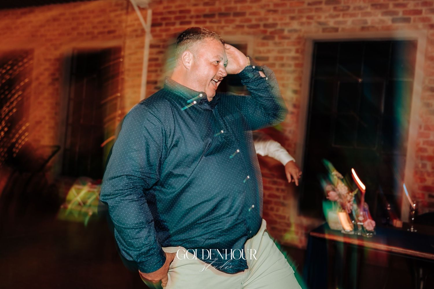Man in teal shirt dancing energetically at an outdoor evening wedding reception.