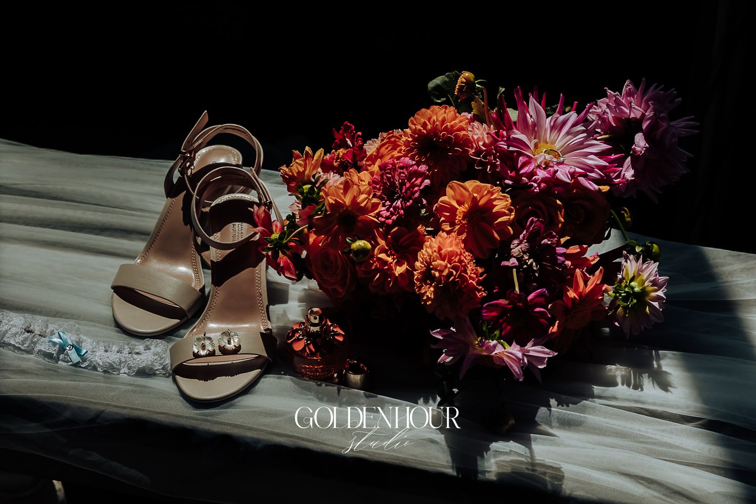 Bridal heels beside vibrant orange and pink floral bouquet on white fabric.