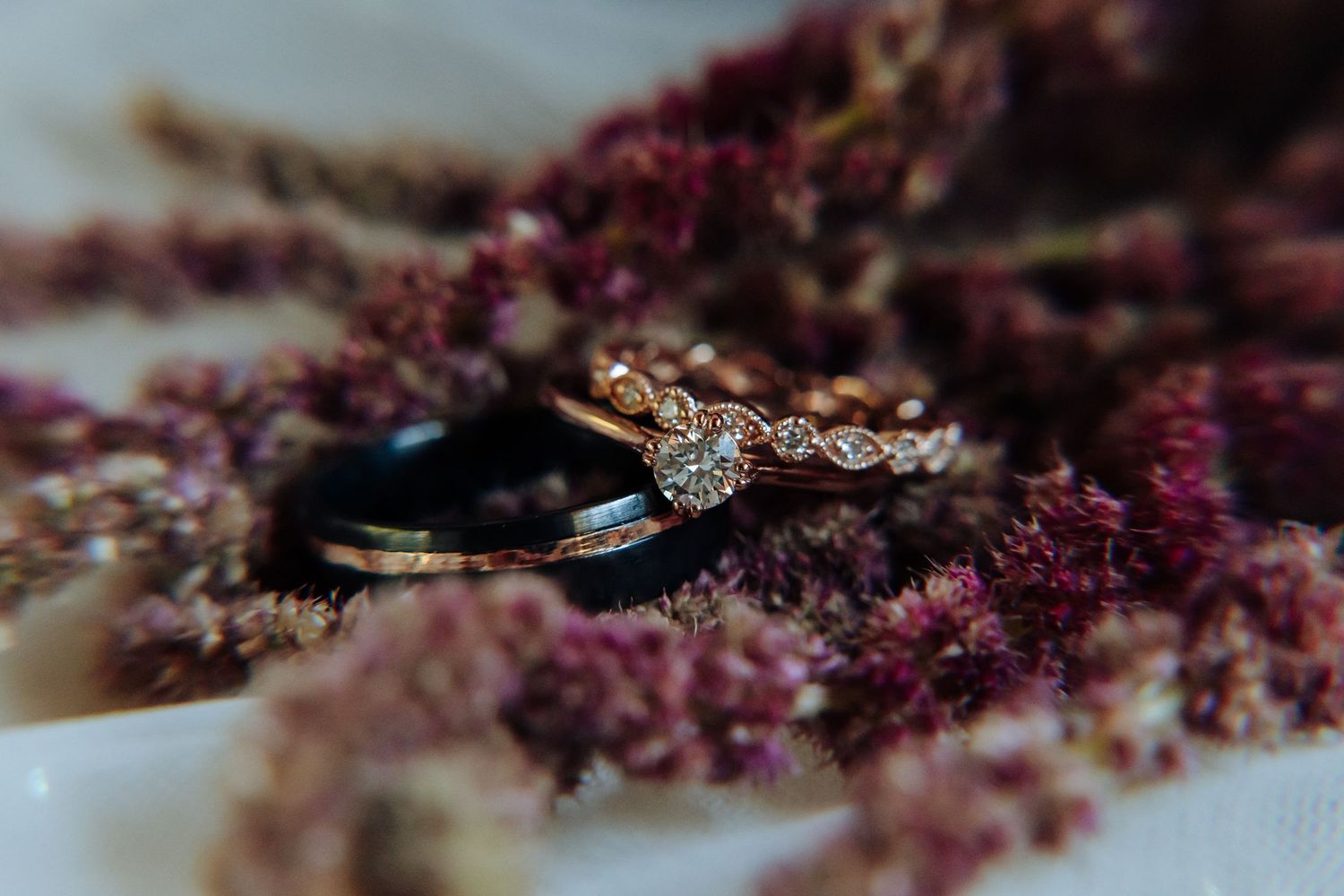 Close-up detail shot of wedding rings resting on purple floral texture.