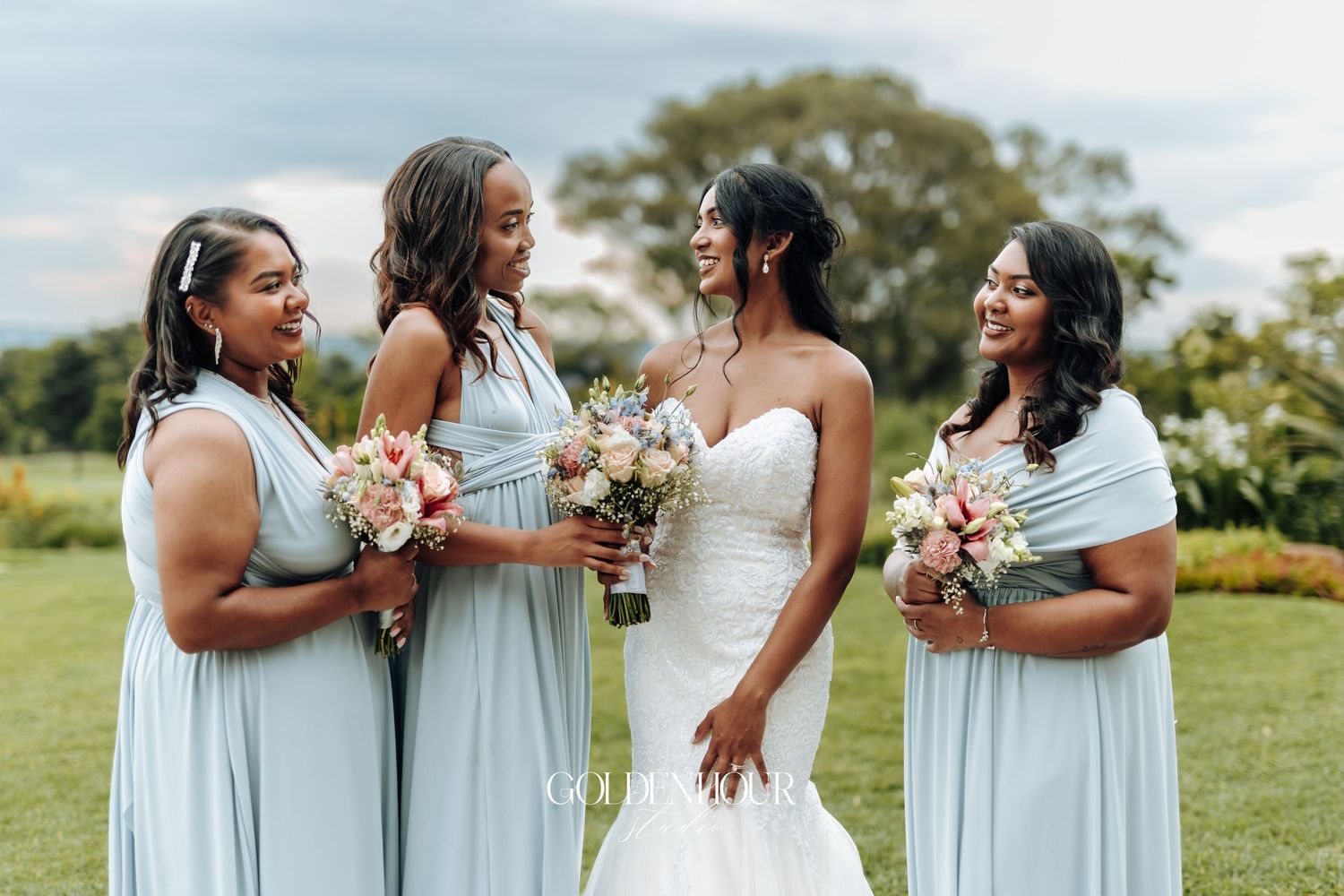 Bridesmaids in light blue dresses holding bouquets while standing together outdoors.