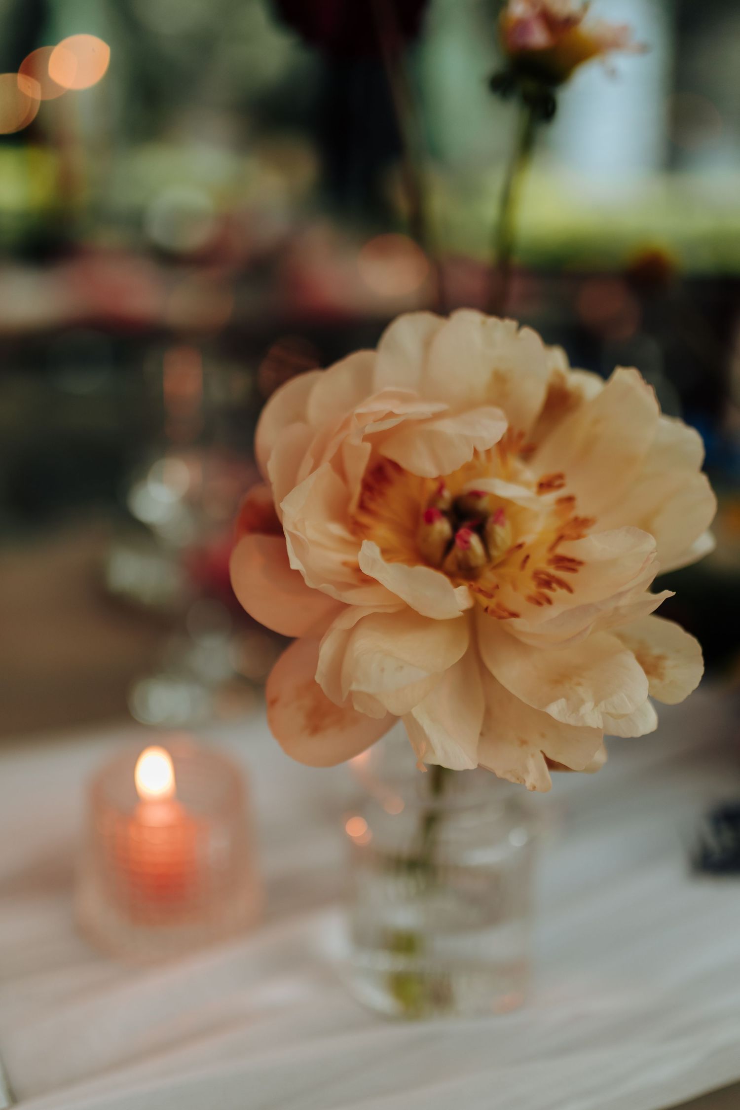 Delicate peach-colored flowers and glowing candles create an elegant table setting at a wedding reception.