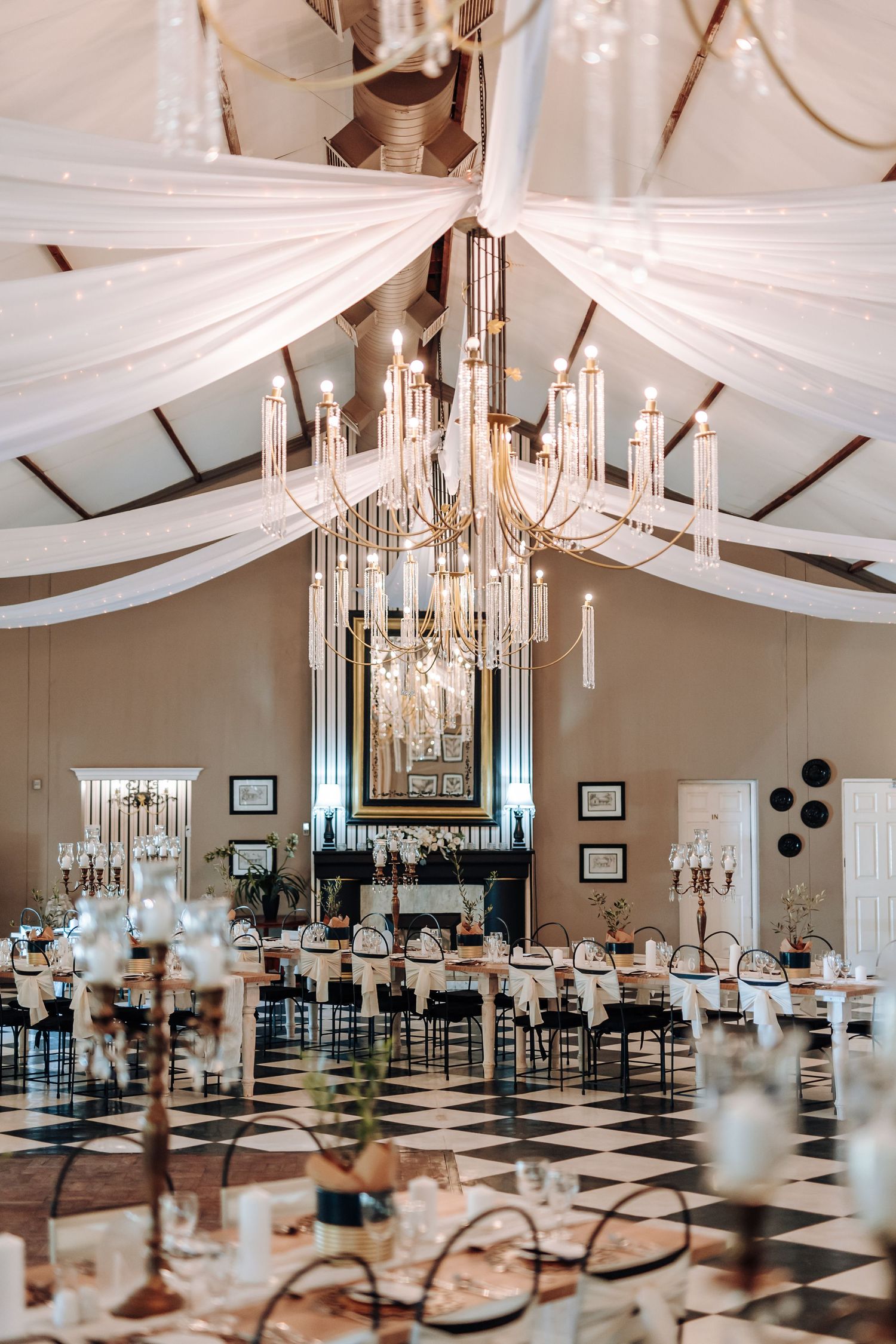 Elegant wedding reception venue with white draped ceiling, crystal chandeliers, and black and white checkered floor.