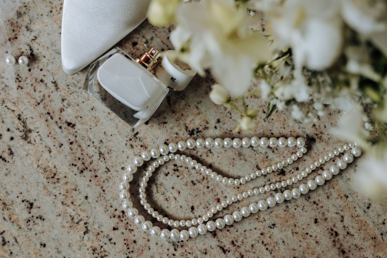 A delicate strand of pearl necklace displayed on a textured surface with white flowers and jewelry box in the background.