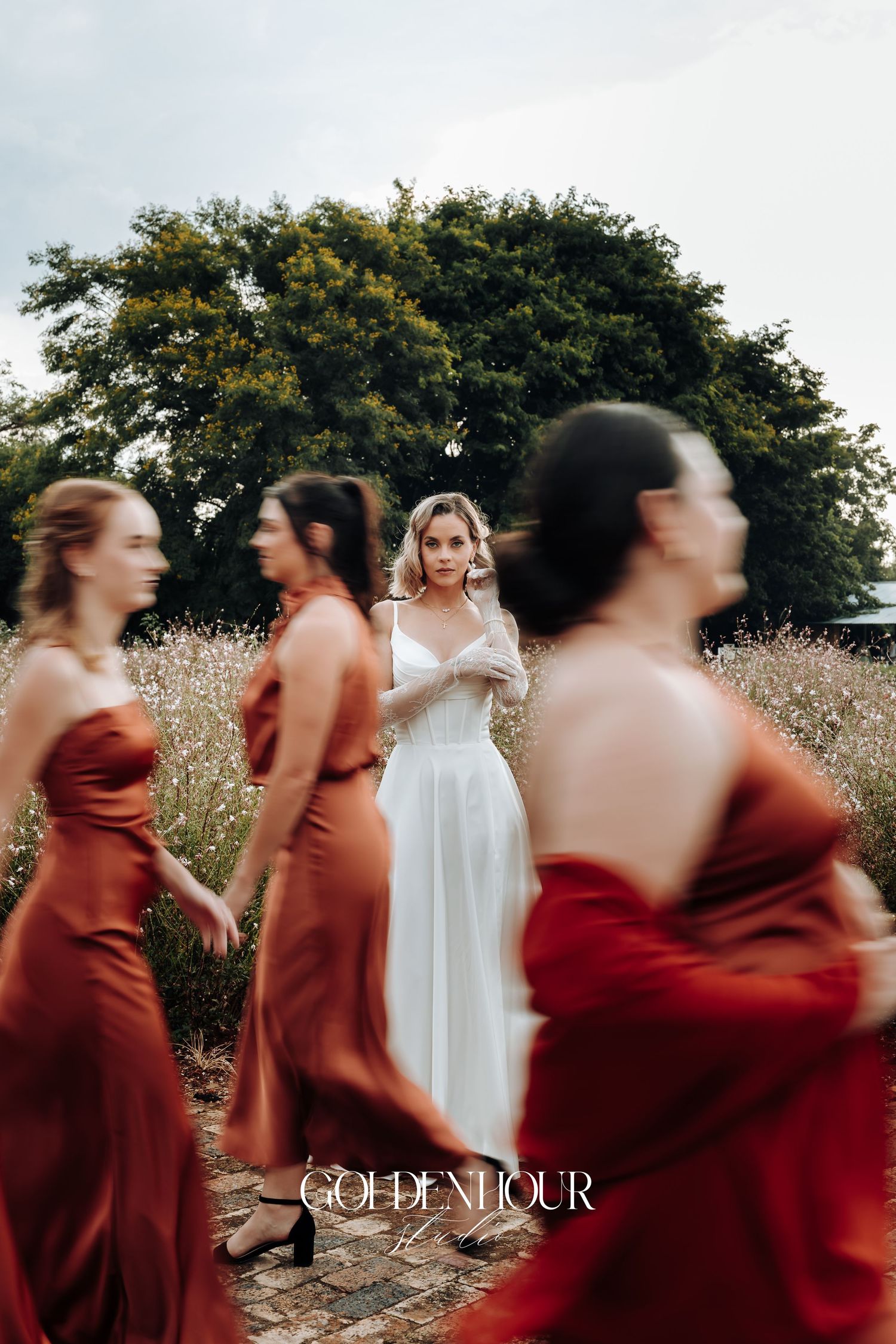 Wedding party in burgundy dresses dances and spins in a garden setting at sunset.
