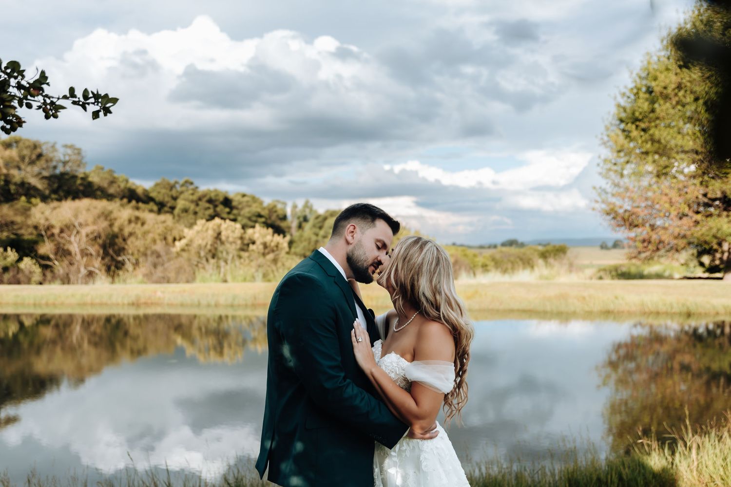 A couple shares romantic moments by a serene lake with autumn trees reflecting in the still waters.