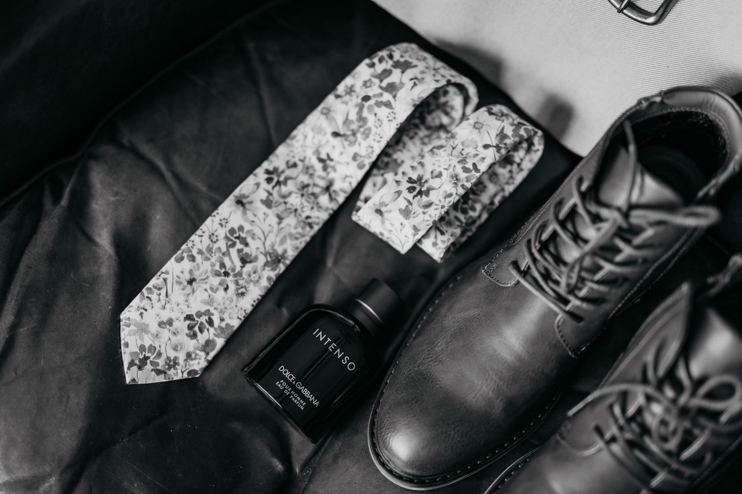 Black and white detail of wedding accessories including floral tie and formal leather shoes.