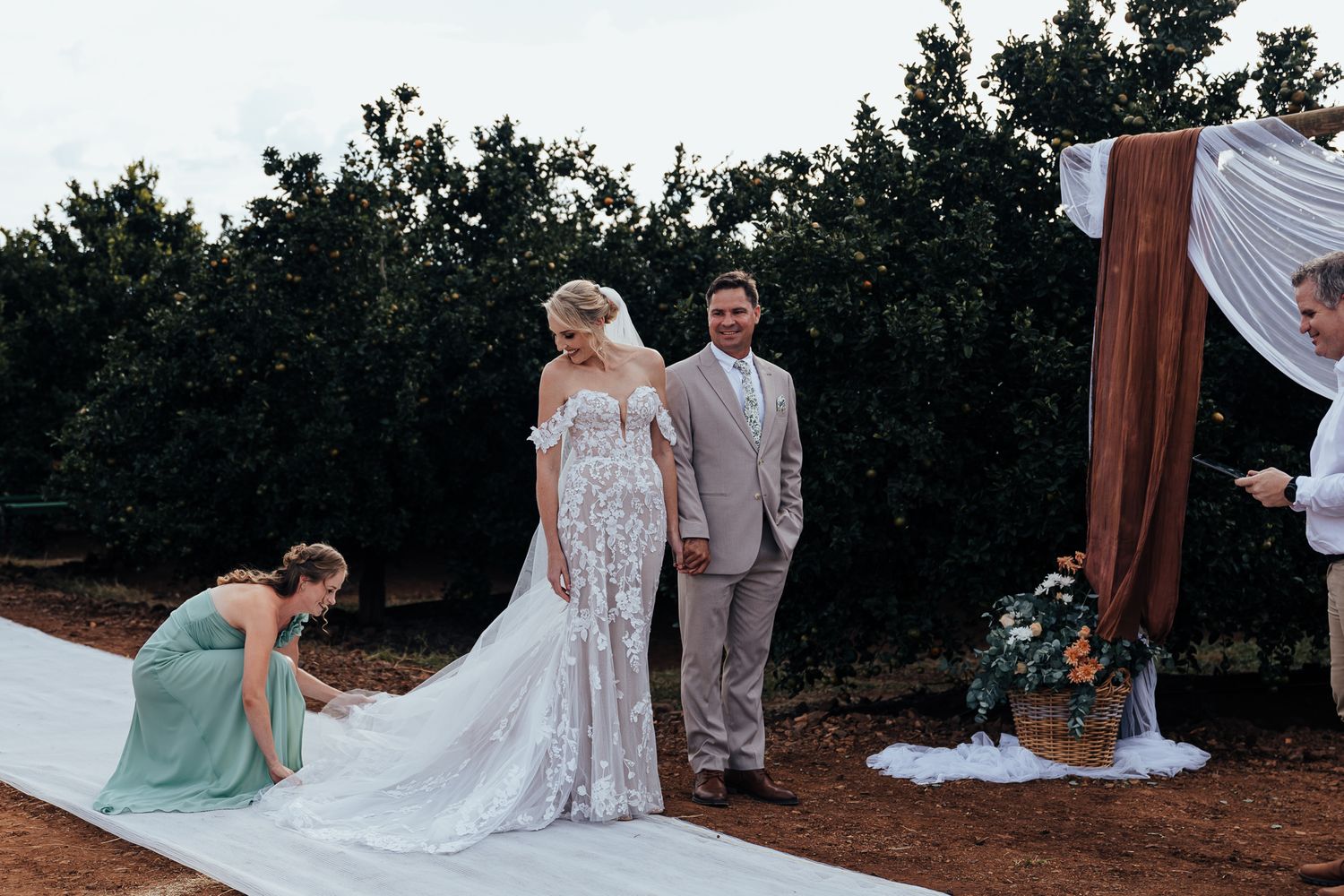 Wedding ceremony setup with floral arrangements and white runner against green foliage backdrop.