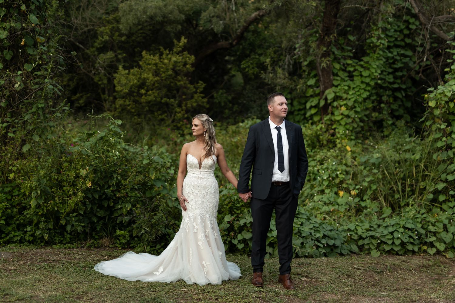 A stylish wedding couple poses in front of a natural woodland backdrop.