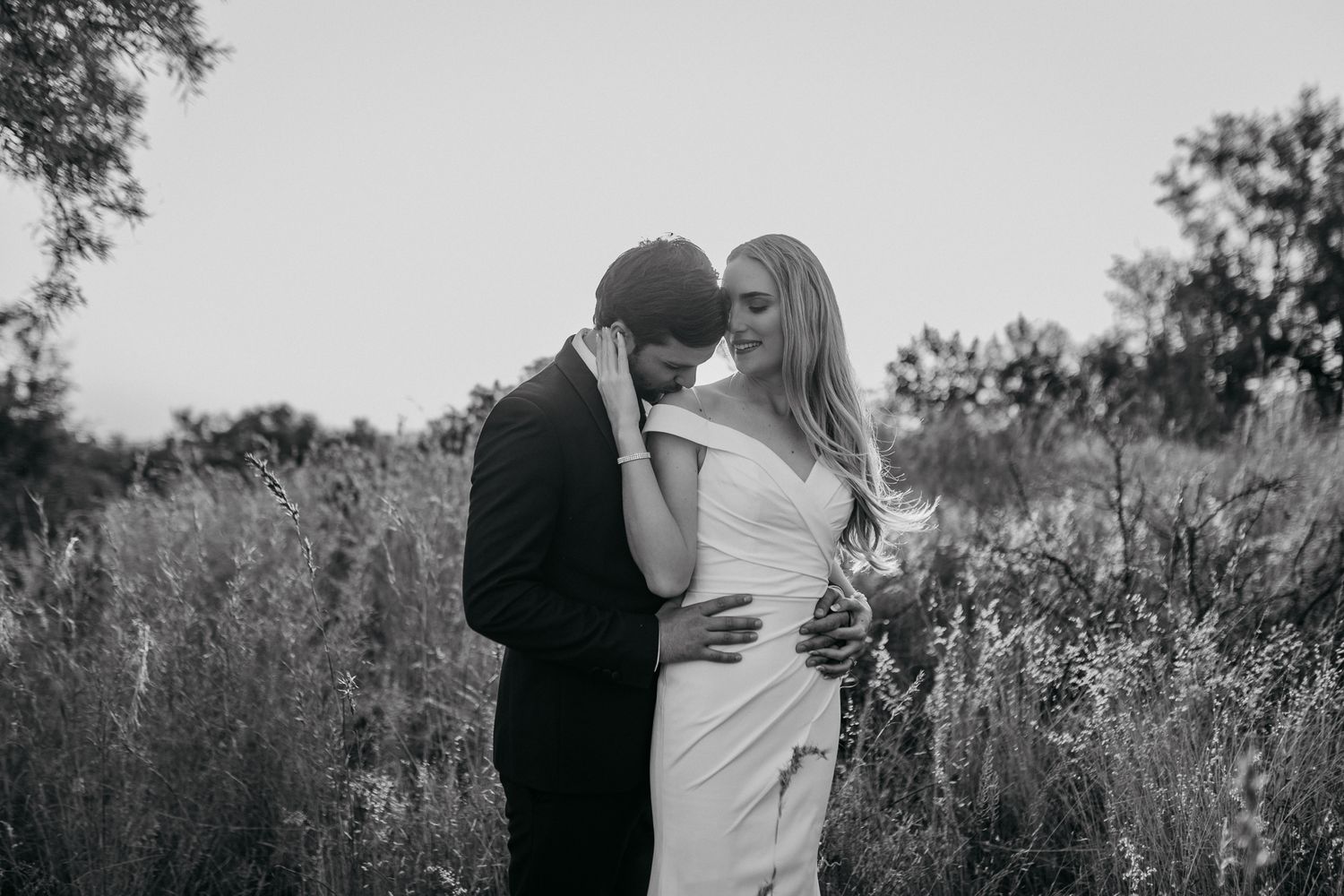 Monochrome wedding portrait in tall grass showing intimate moment between newlyweds.