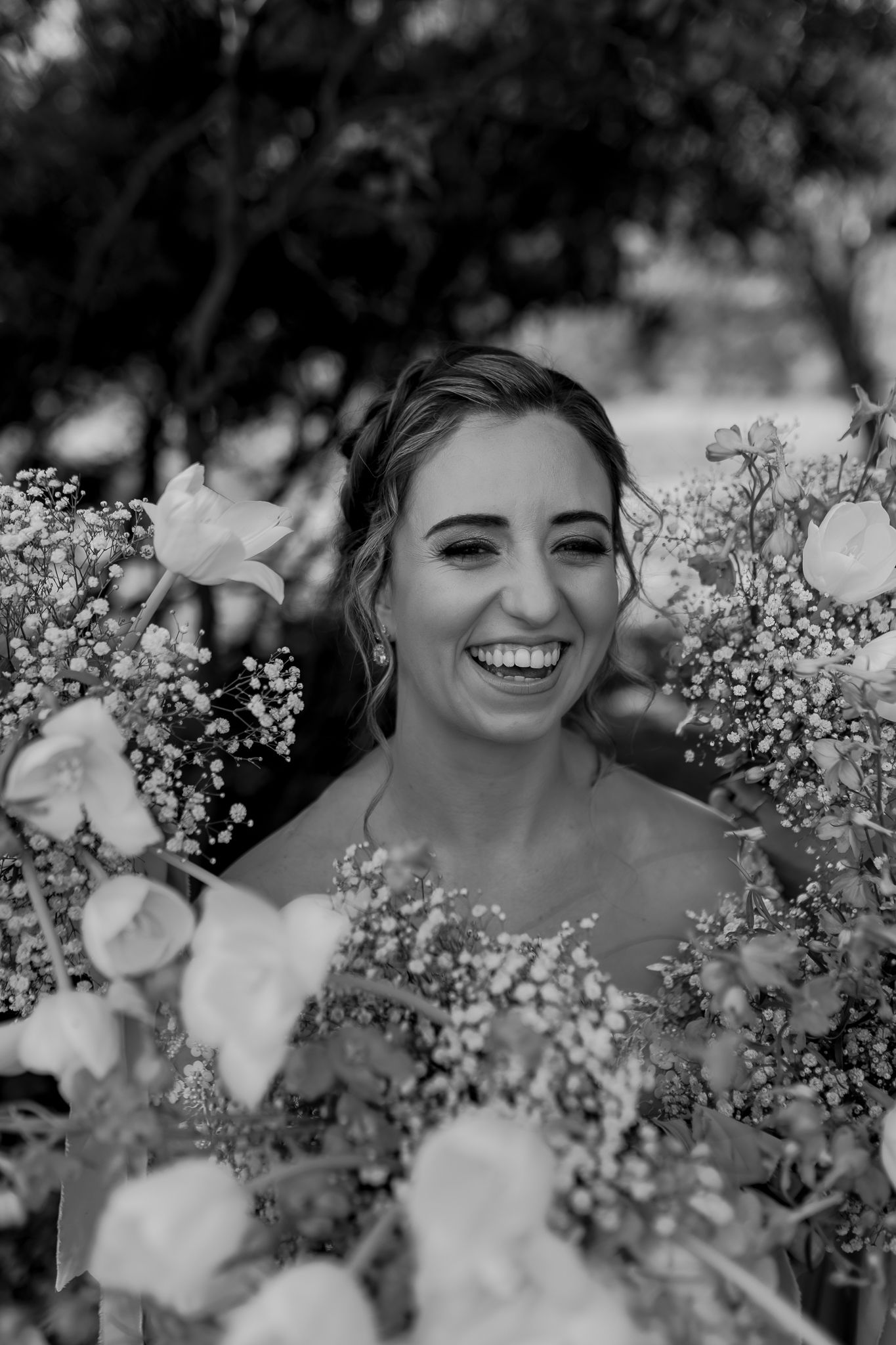A black and white portrait of a joyful bride surrounded by white flowers and baby's breath.