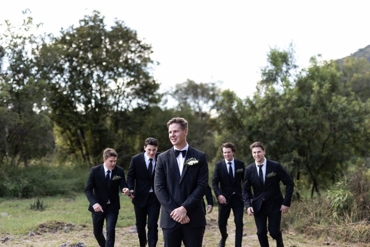 Wedding party walking through a field with mountains visible in the background.