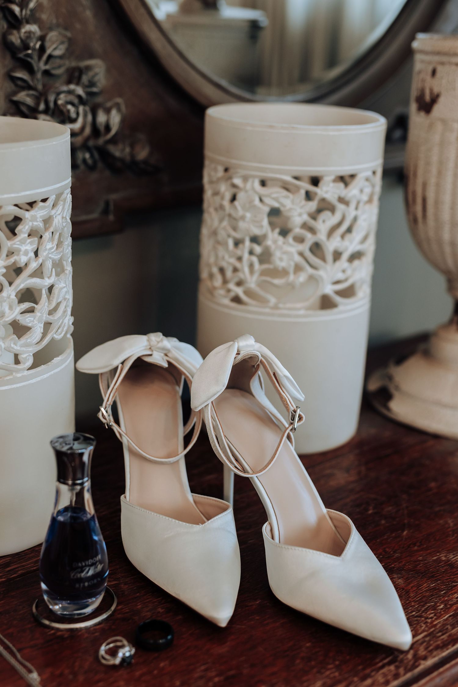 Elegant white bridal shoes with ankle straps displayed next to decorative ceramic containers on wooden surface.