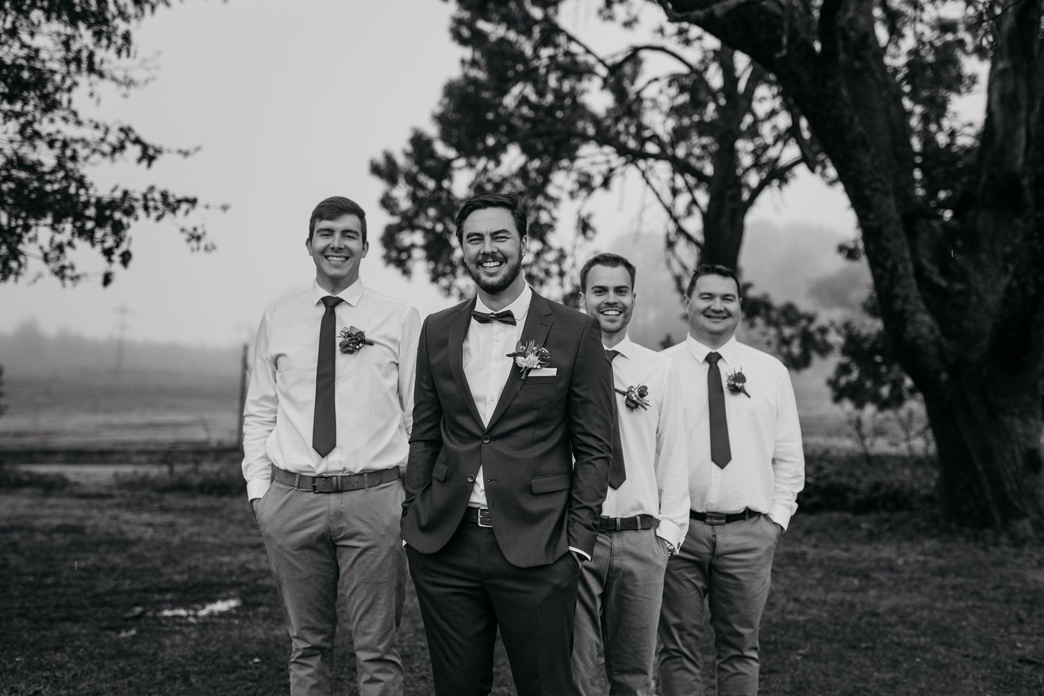 Black and white portrait of wedding party standing together under a tree.