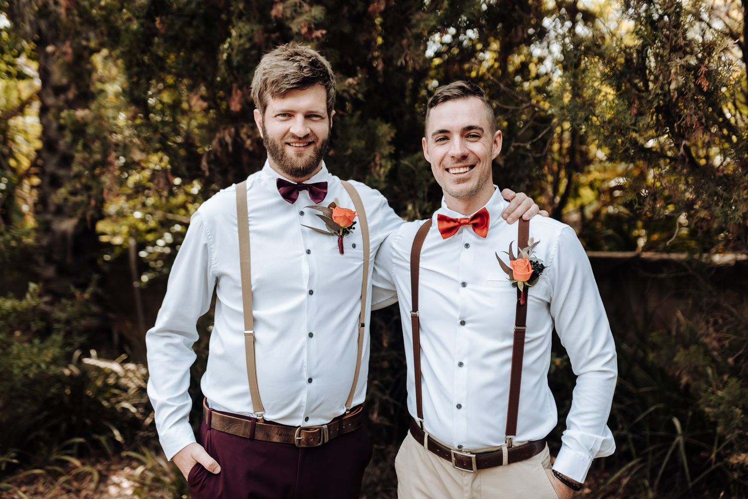Groomsmen wearing suspenders and bow ties pose together in a wooded outdoor setting.