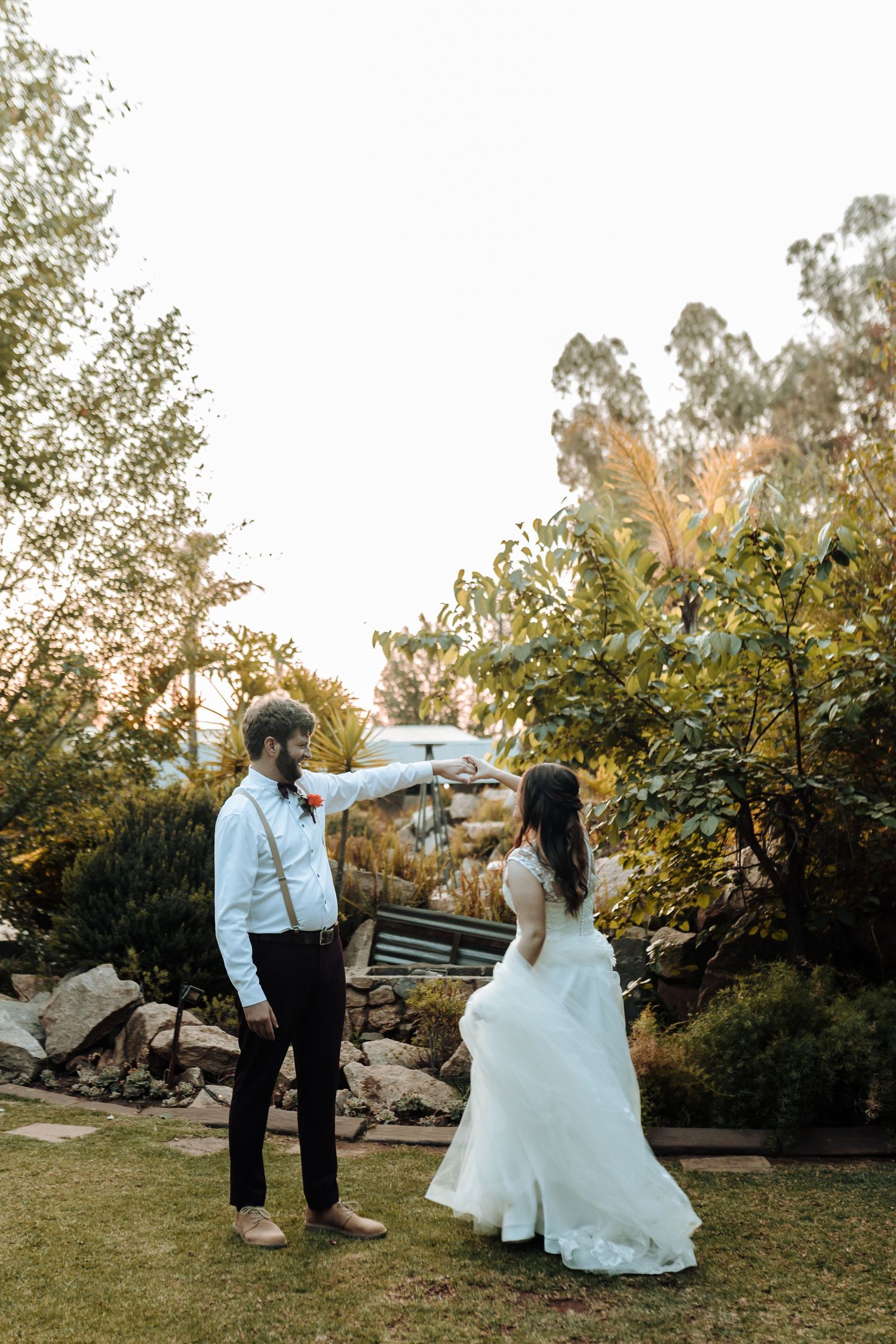 Playful wedding couple dancing in garden setting during golden hour.