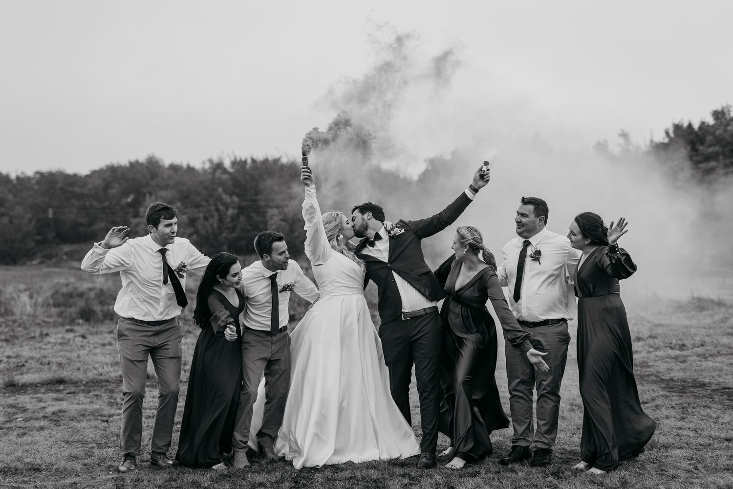 Black and white photo of wedding party celebrating with smoke bombs outdoors.
