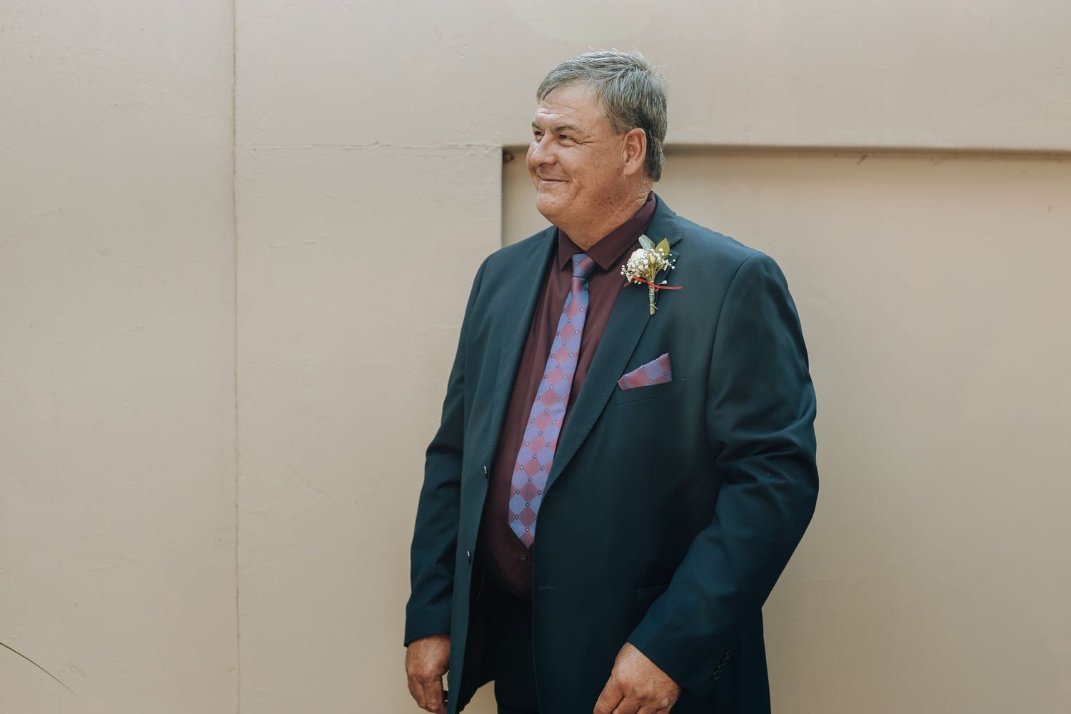 A formal portrait of someone wearing a navy suit with pink tie and boutonniere.