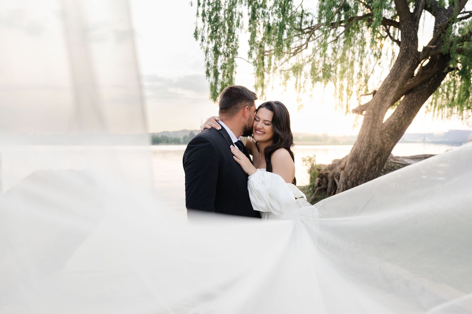 A romantic wedding photo under a willow tree with the bride's flowing white dress billowing in the breeze.